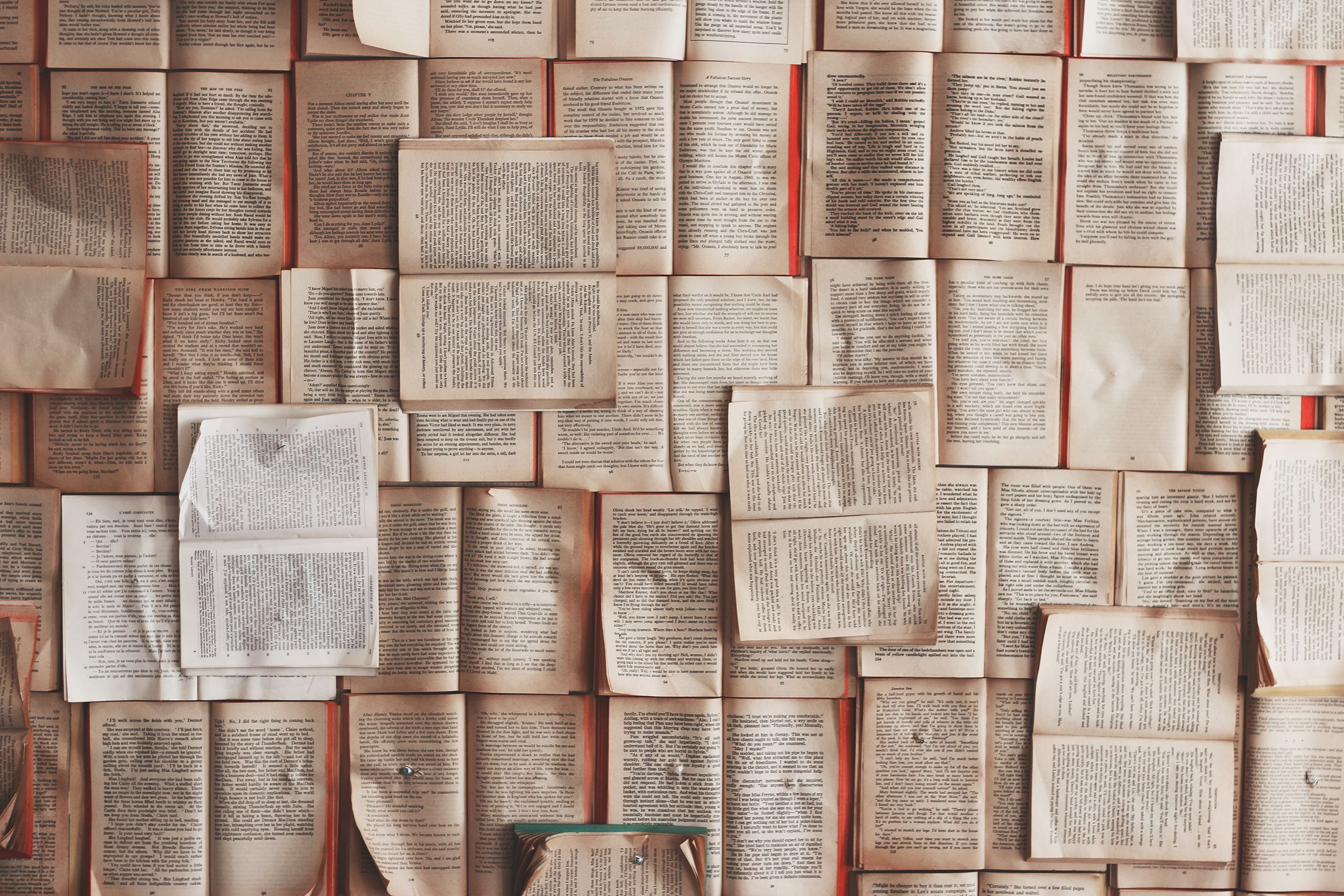 Old books laid out on top of each other with the pages open to create a carpet of mismatched pages.