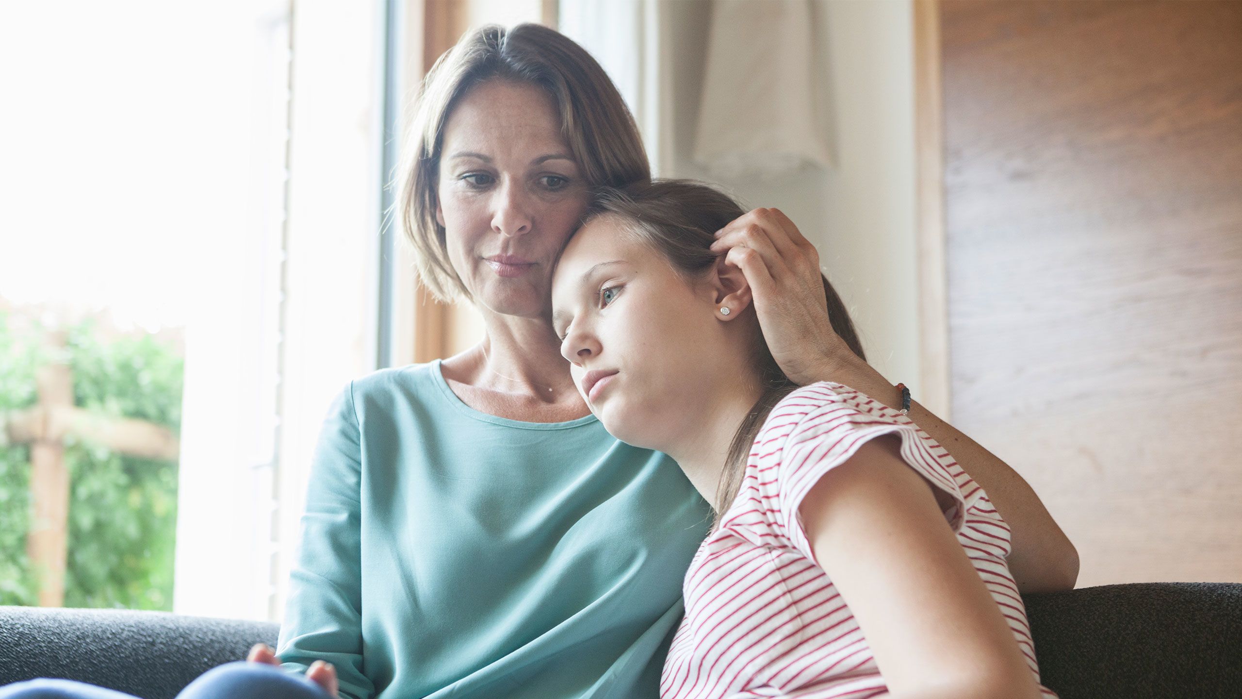 Mother comforting daughter sitting on sofa.