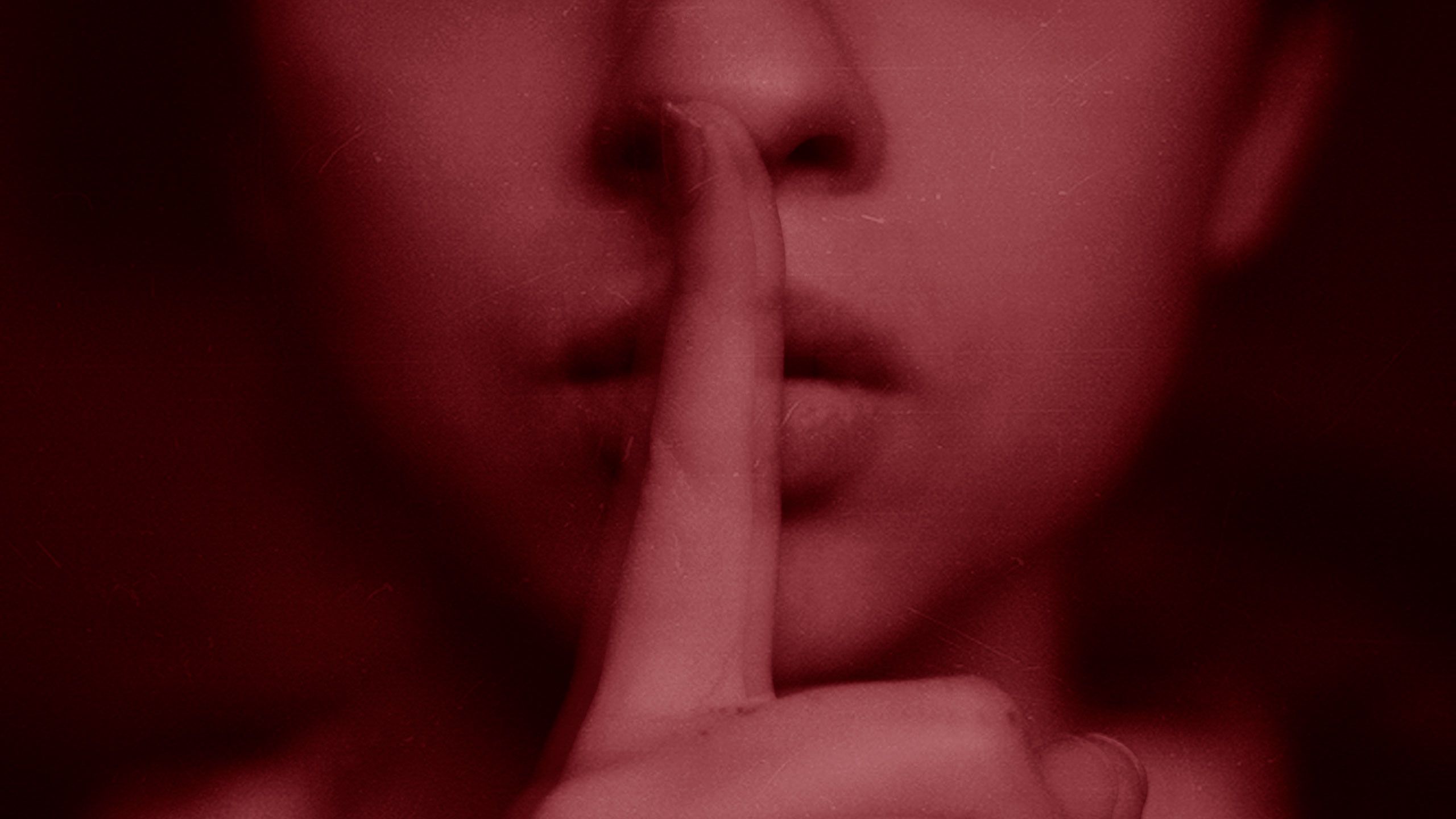 An image of a woman holding a finger over her mouth indicating to be quiet.