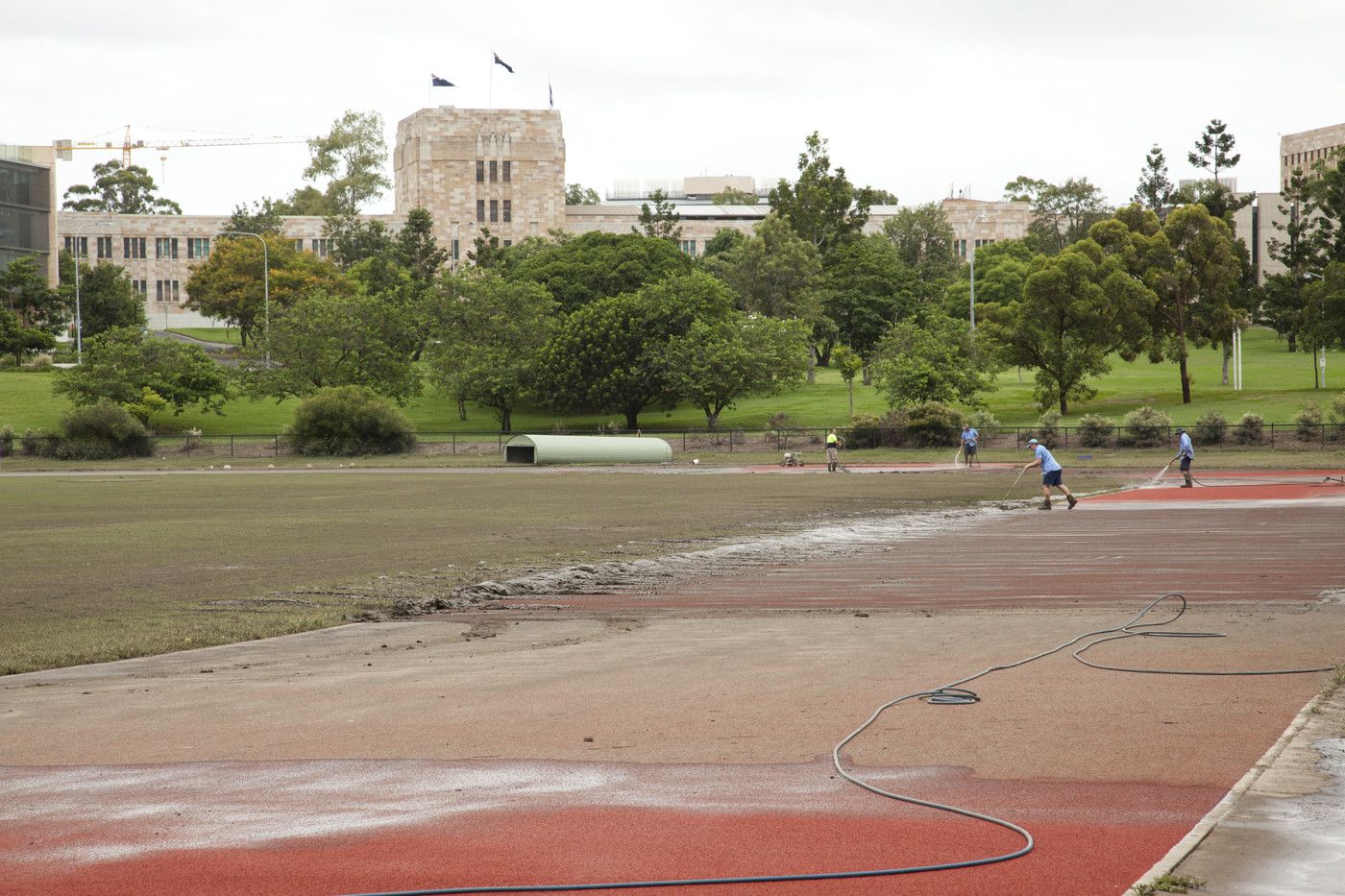 An image of ground staff cleaning the mud from the UQ Athletics Centre.