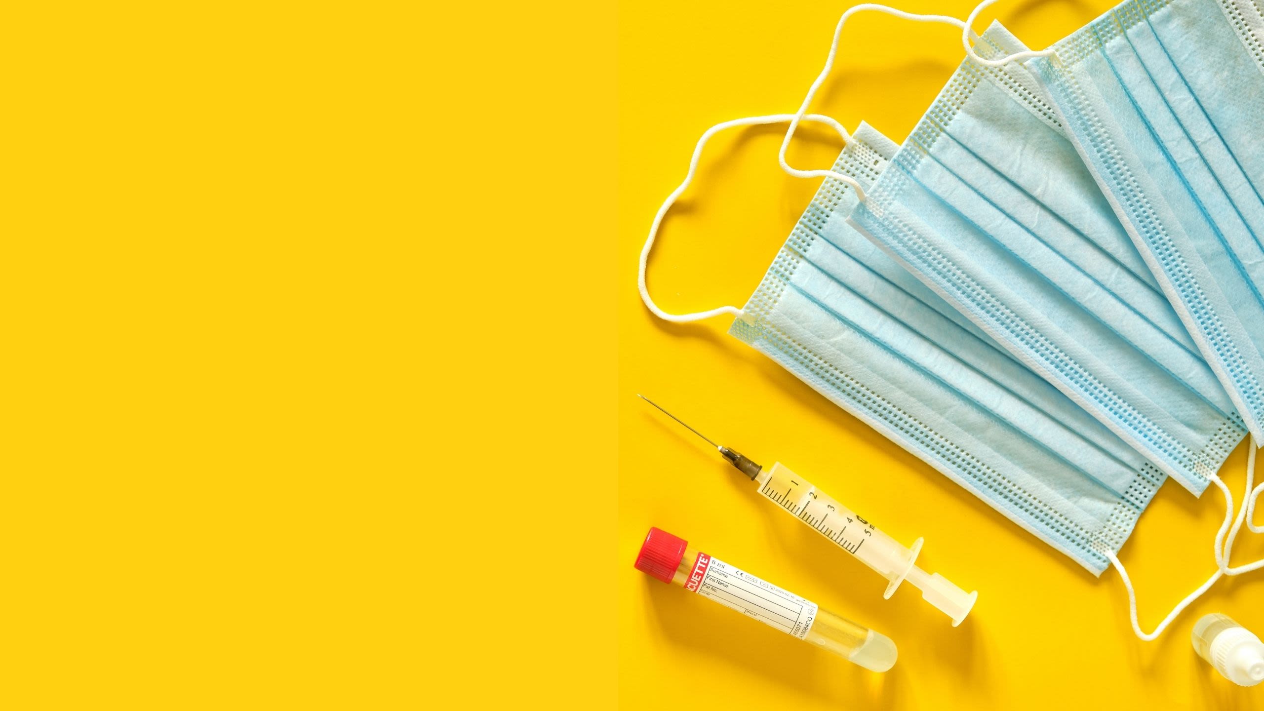 Blue medical protective mask and syringe on yellow background.