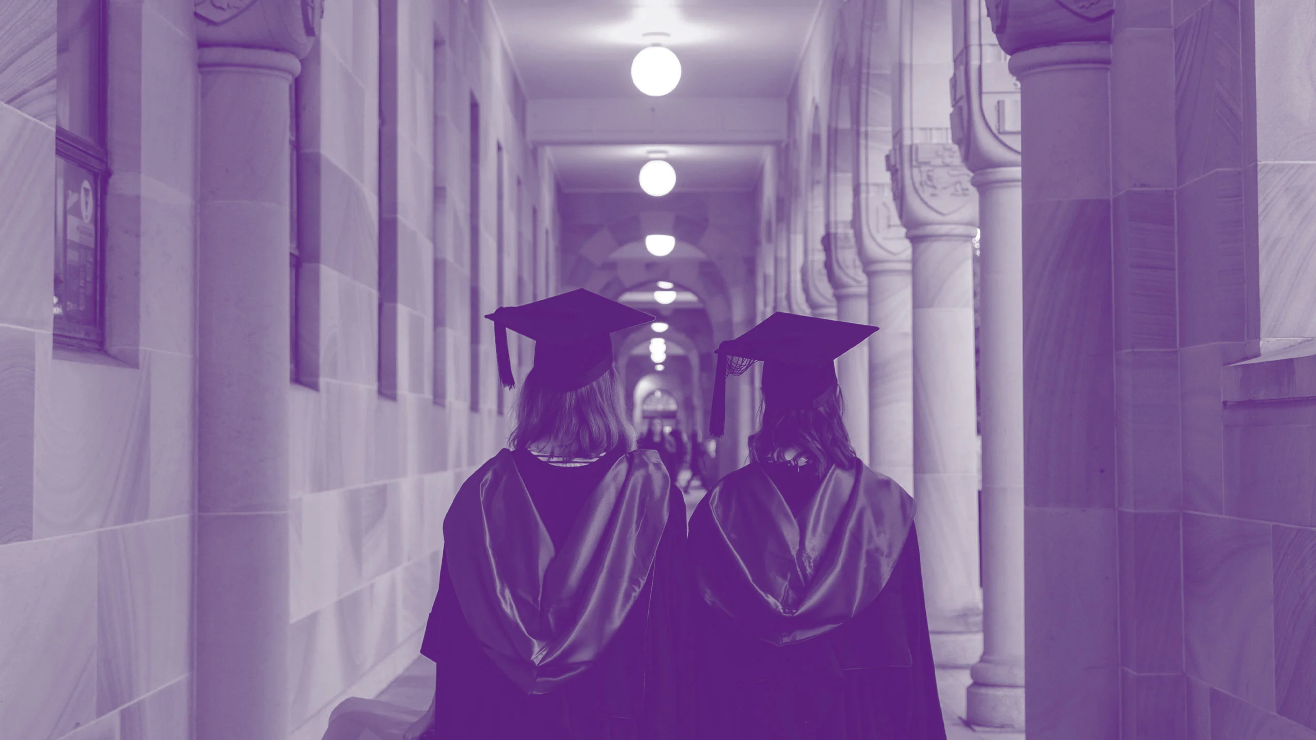 An image of two graduates wearing cap and gowns, walking through the cloisters of UQ's Great Court. walking