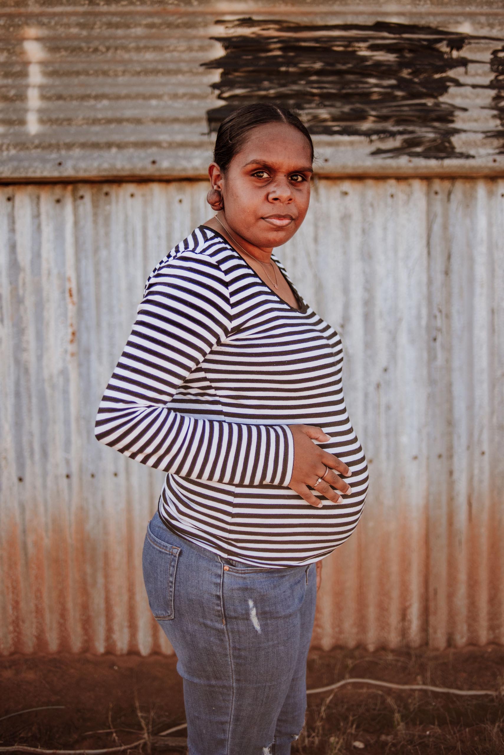 Photograph of woman in a long sleeve black and white striped shirt with a corrugated iron wall behind her.