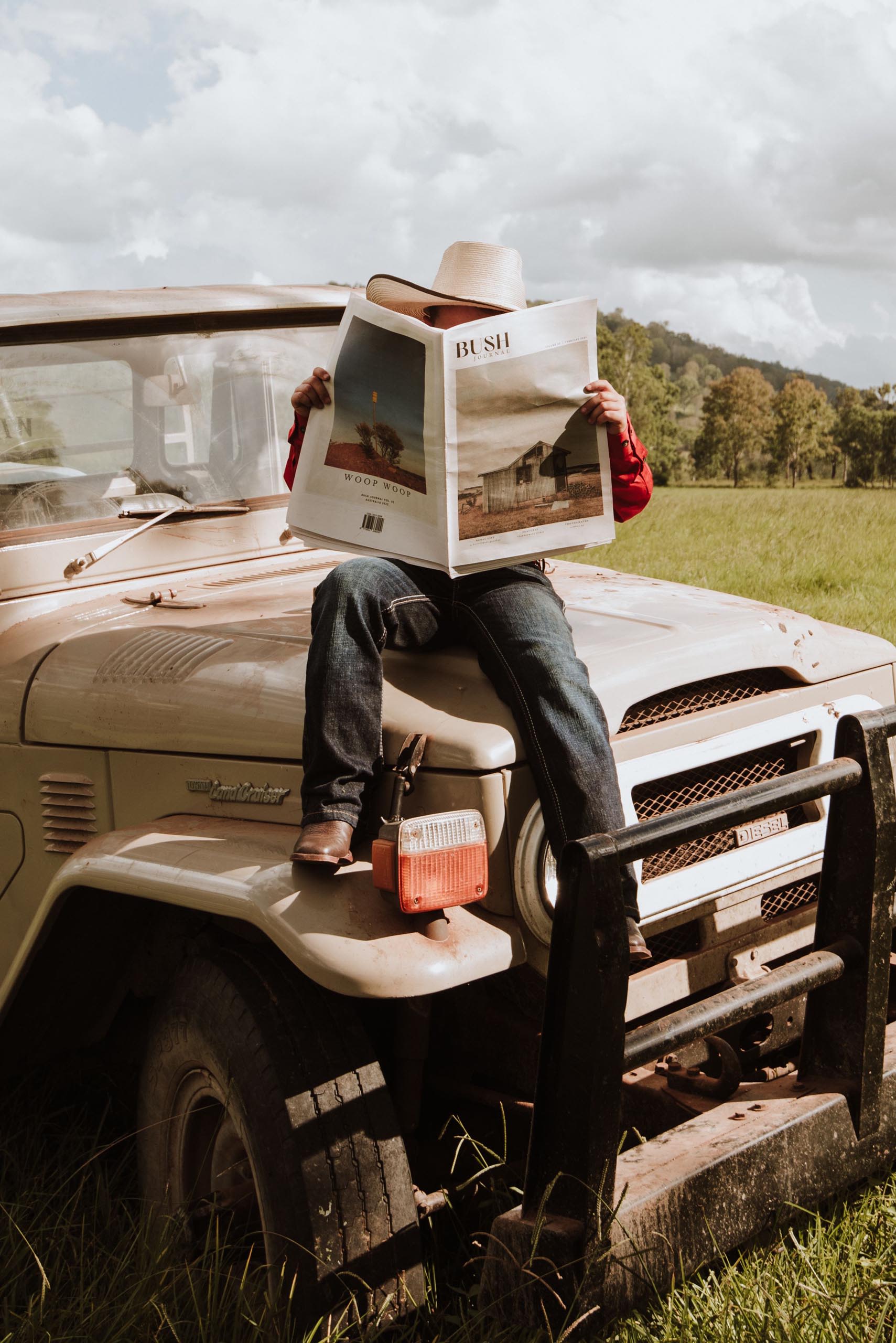Man reading Bush Journal and sitting on a truck with a hill in the background.