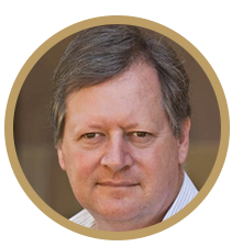 A circle portrait of a man smiling into the camera. He has dark hair and eyes.
