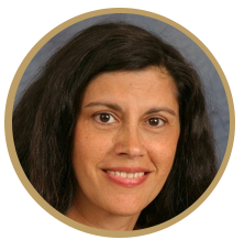 A circle portrait of a woman smiling into the camera. She has dark hair and eyes.