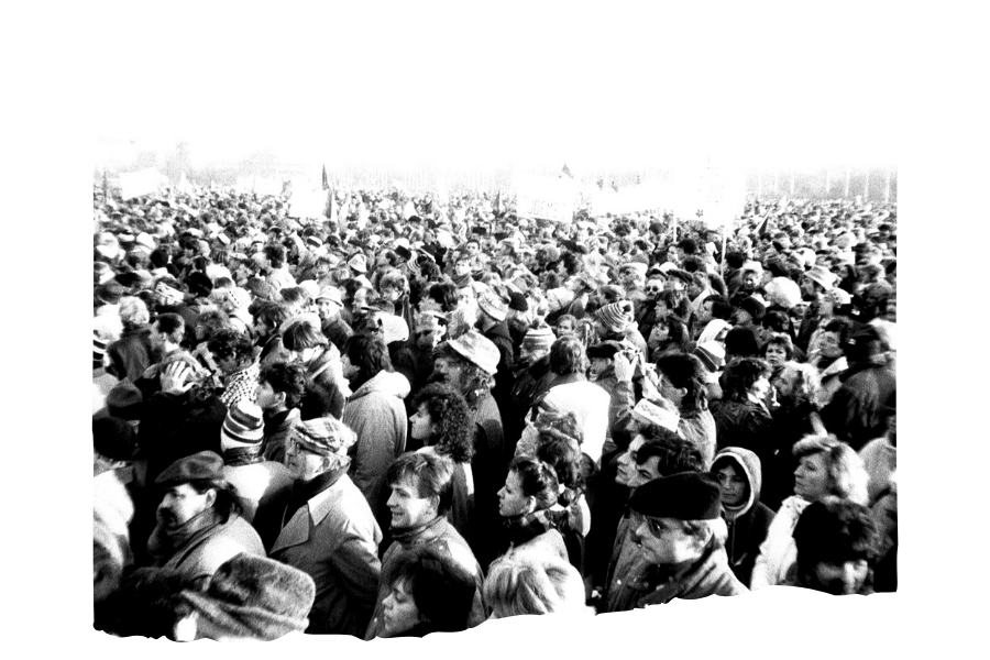 A black-and-white photo designed to look torn. A huge crowd of people are facing in one direction. There are some unreadable signs being held in the background.