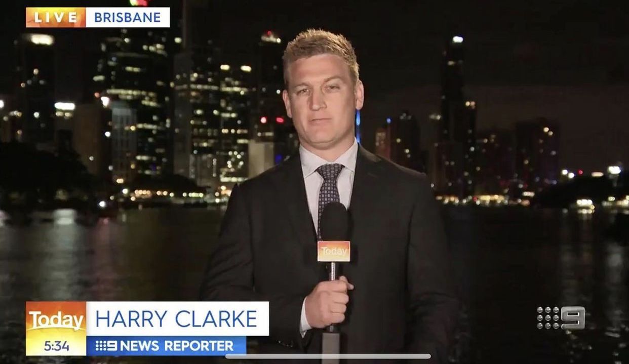 Harry Clarke standing in front of the Brisbane River at night holding a microphone