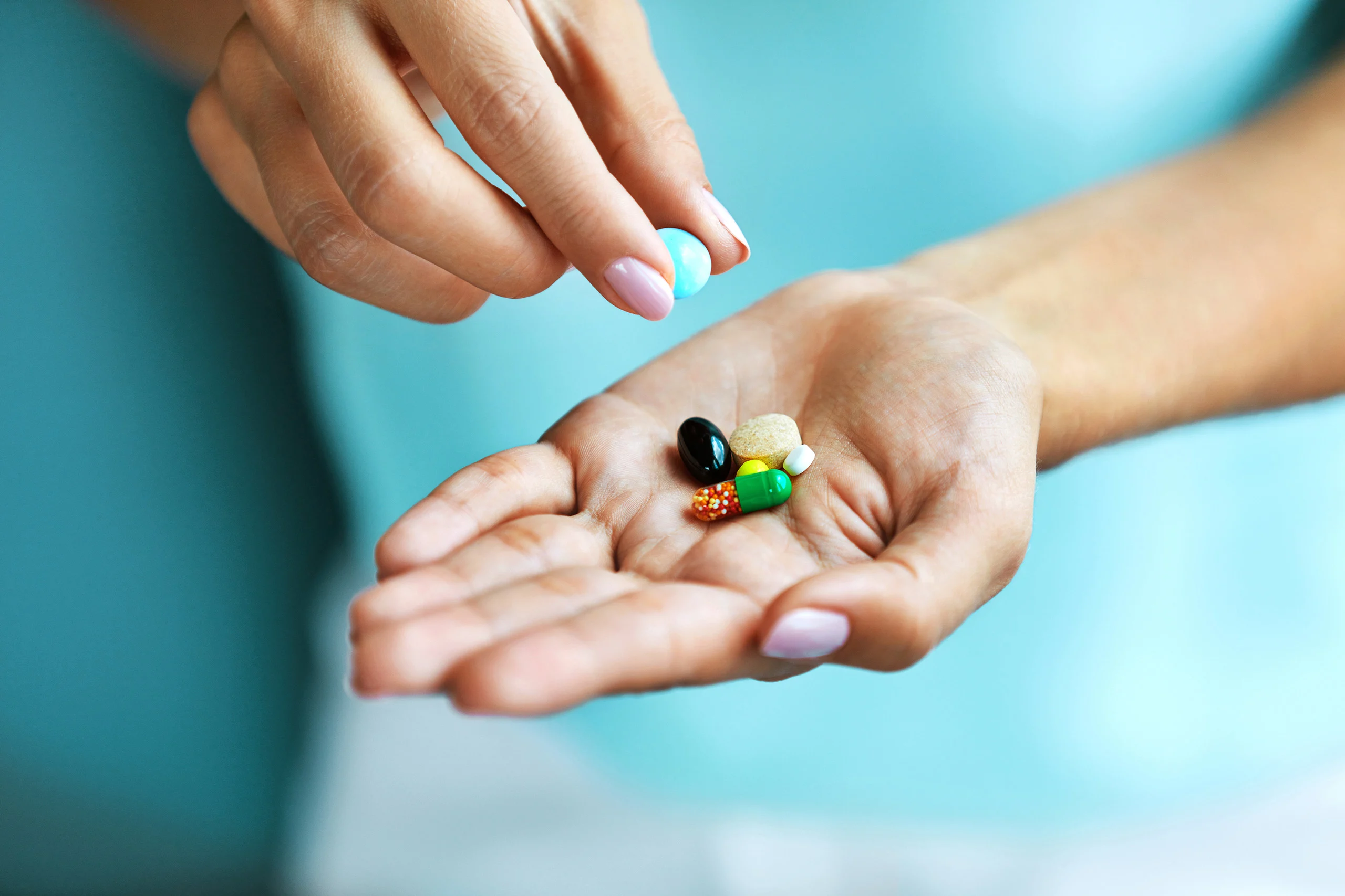One hand containing several vitamin tablets and another holding one tablet in its fingers