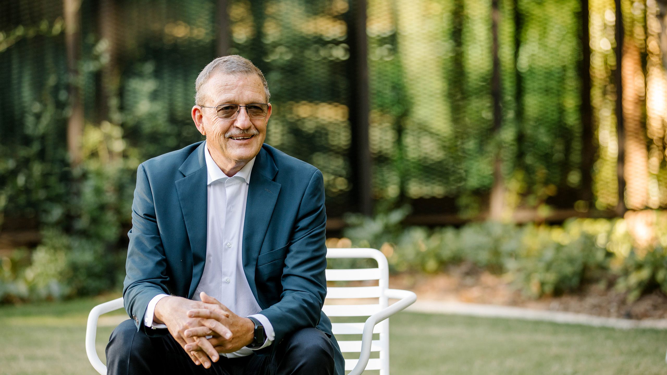 Bob Christiansen sitting on a chair smiling with hands crossed together in front of him..