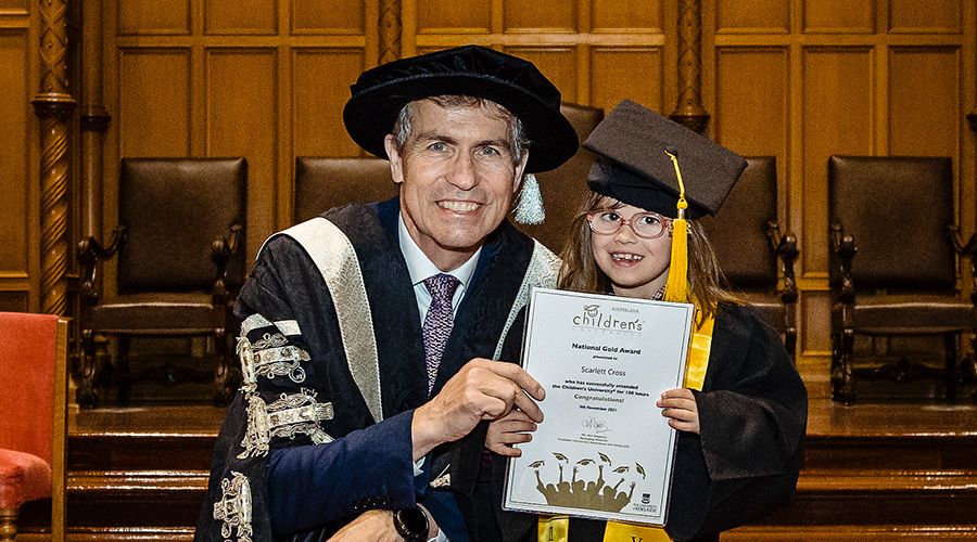 Peter Høj and a child in graduation attire holding a certificate for the Children's University.
