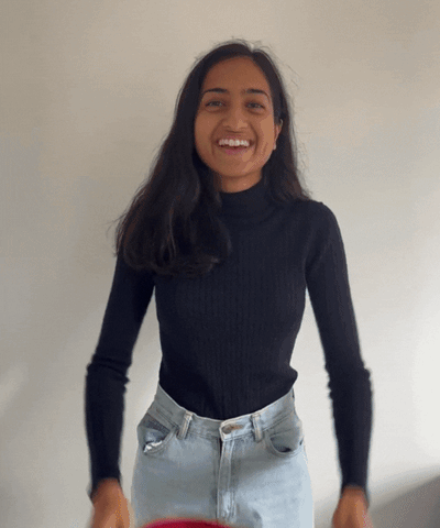 A GIF of a woman in blue jeans and a black turtleneck trying on colourful fabric hats.