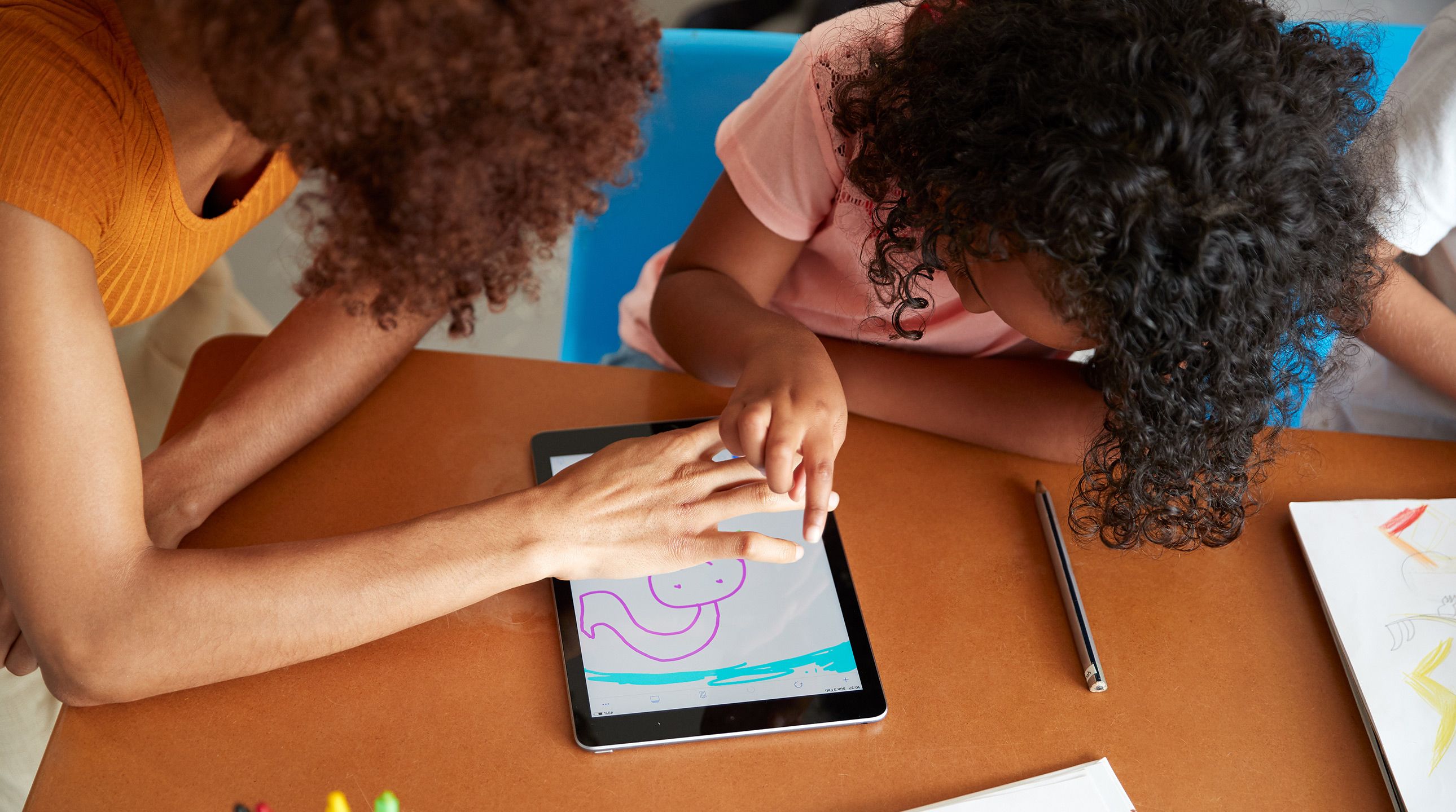 Primary school teacher and pupil drawing on a digital tablet together in the classroom.