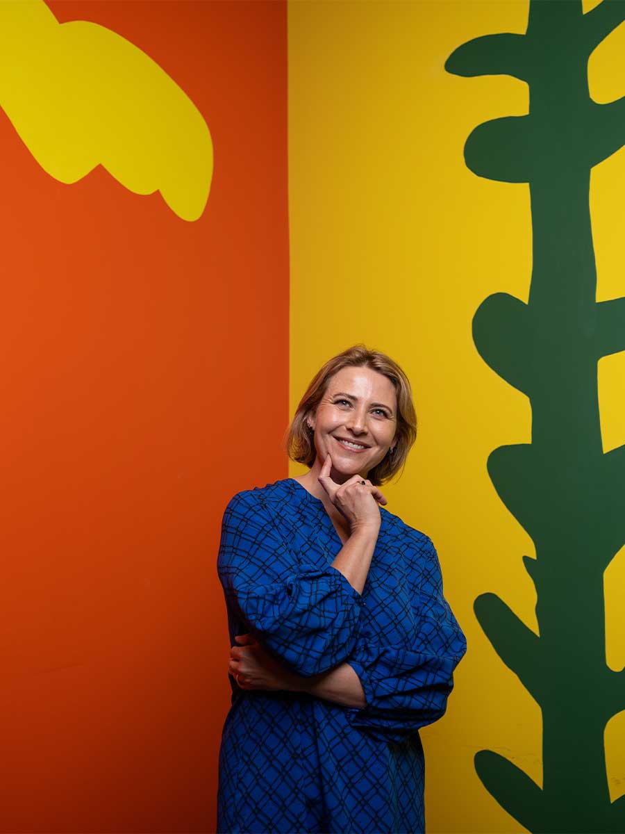 A sequence of three images of Children’s Gallery Coordinator Jodi Ferrari posing in front of a colourful wall space inside the Children's Gallery at HOTA.