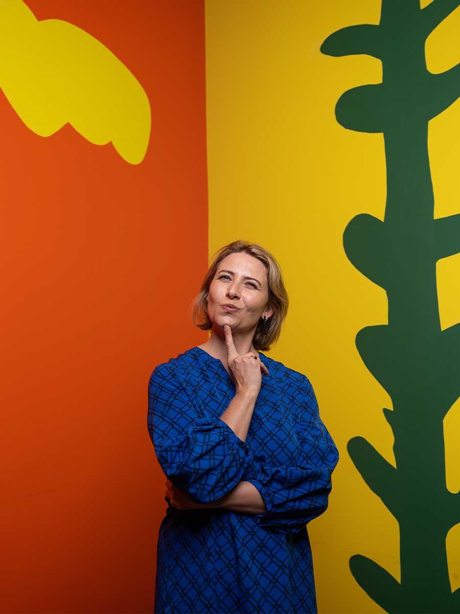 A sequence of three images of Children’s Gallery Coordinator Jodi Ferrari posing in front of a colourful wall space inside the Children's Gallery at HOTA.