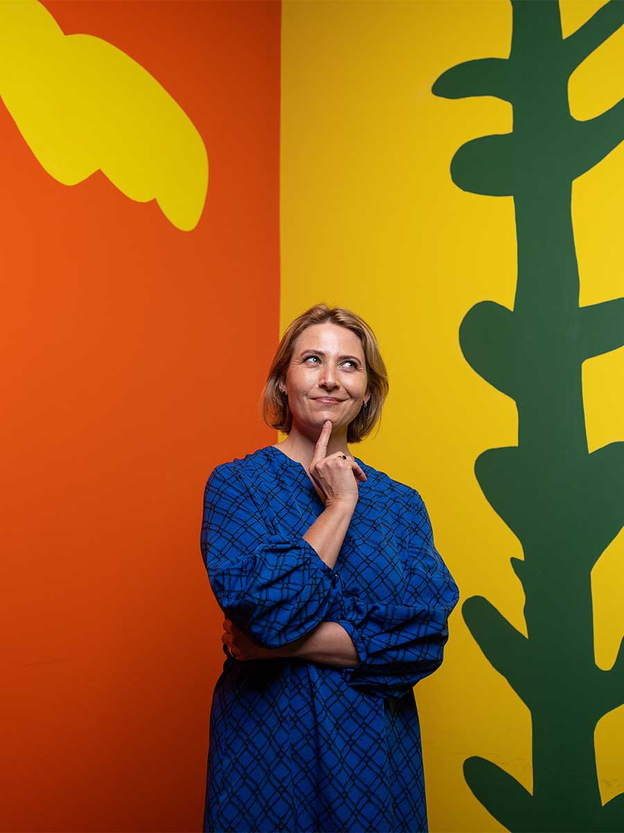 A sequence of three images of Children’s Gallery Coordinator Jodi Ferrari posing in front of a colourful wall space inside the Children's Gallery at HOTA.