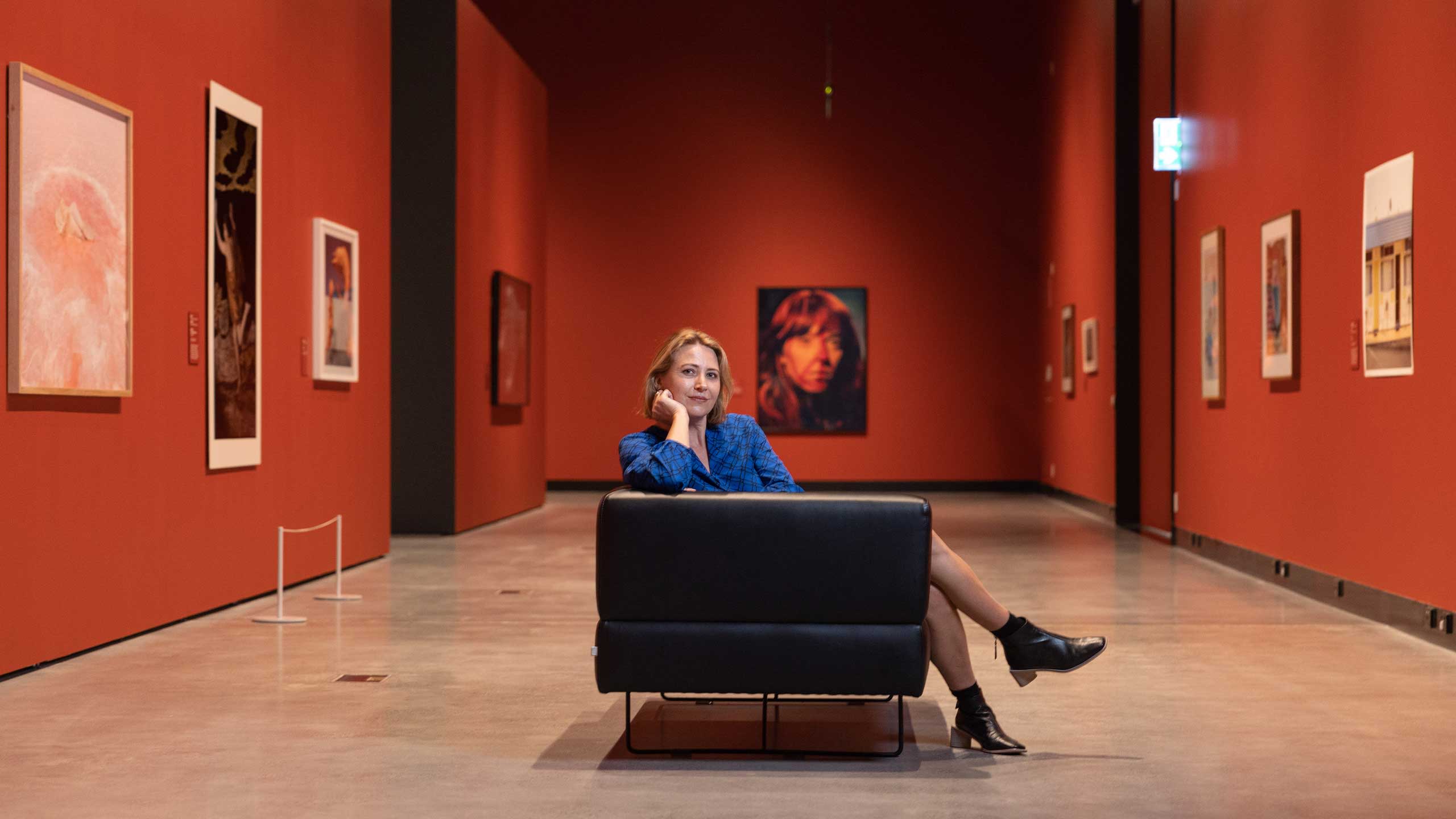 An image of HOTA Children’s Gallery Coordinator Jodi Ferrari sitting on a chair inside the HOTA Gallery.