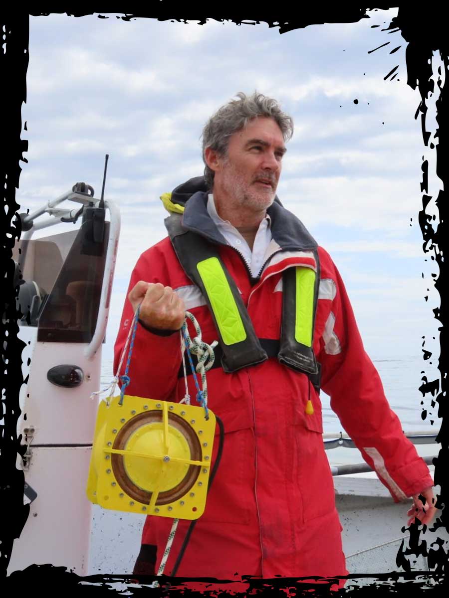 An image of Professor Michael Noad holding a speaker to emit sound frequencies into the ocean.