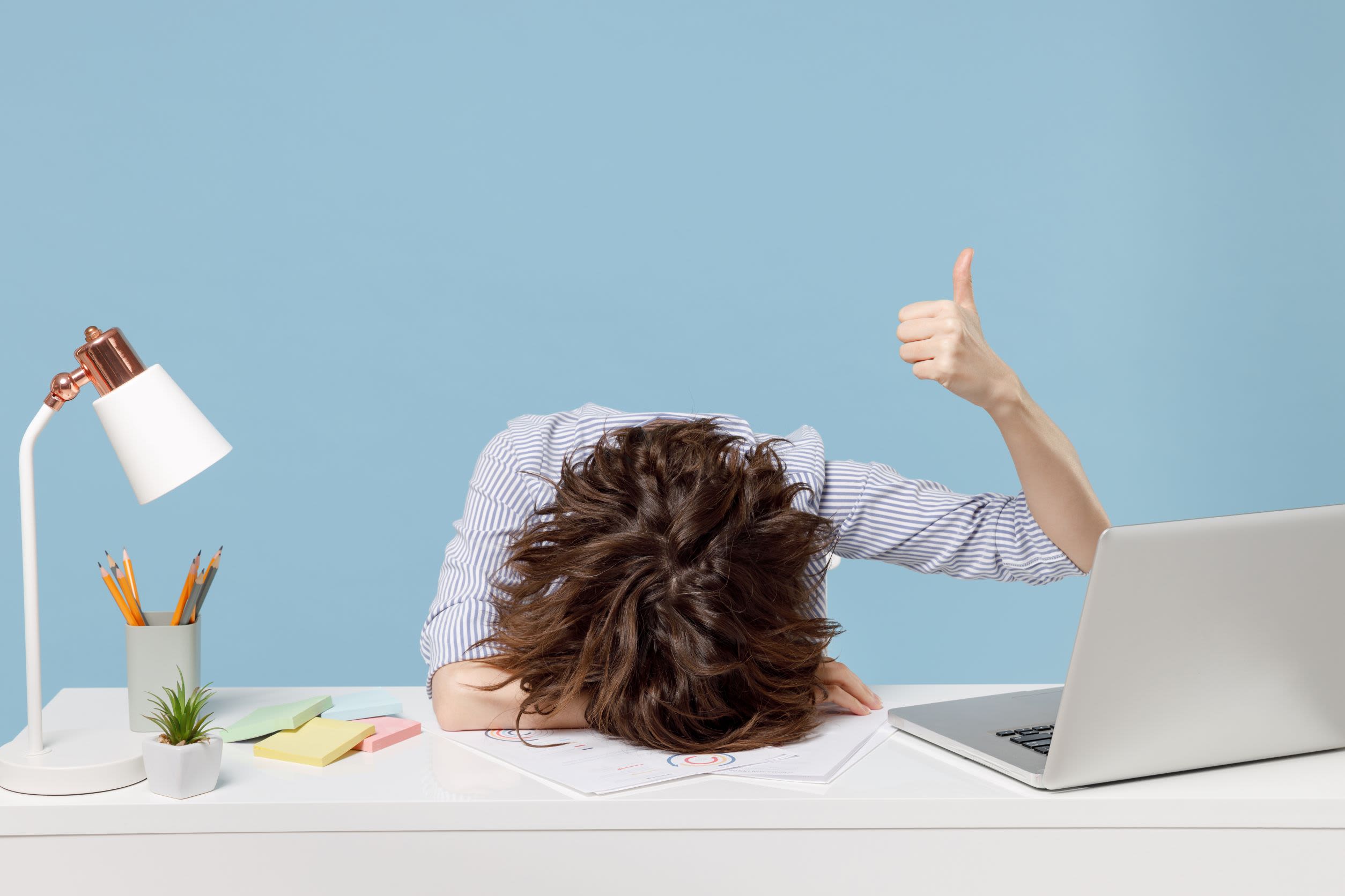 A woman with her head on a desk and thumb up