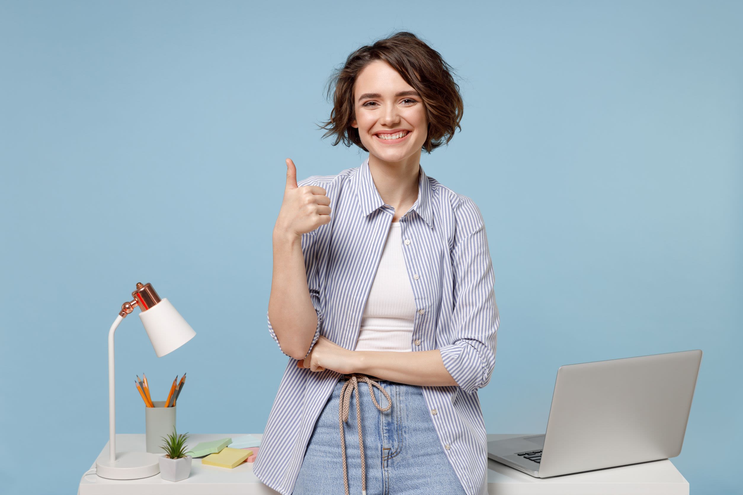A woman smiling on her desk giving a thumbs up