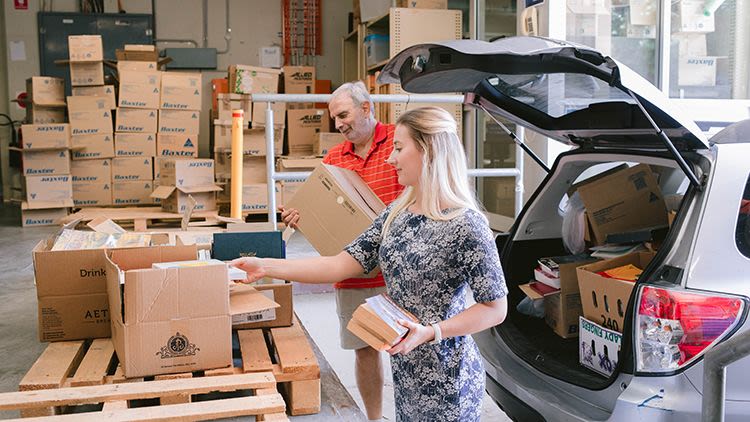 Two volunteers unstack boxes of books from the boot of a car.