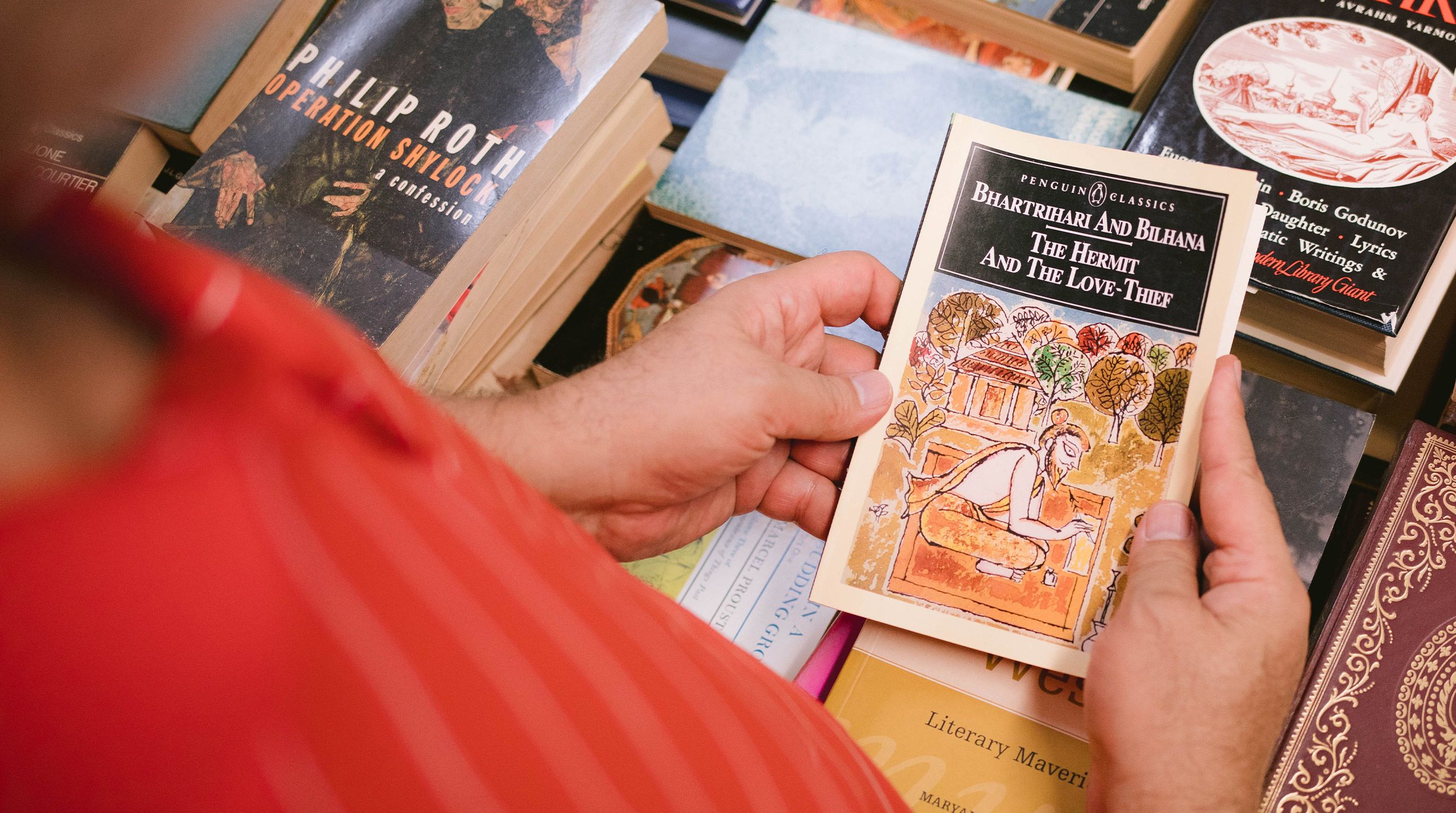 An old book held by two hands over a stack of other old novels.