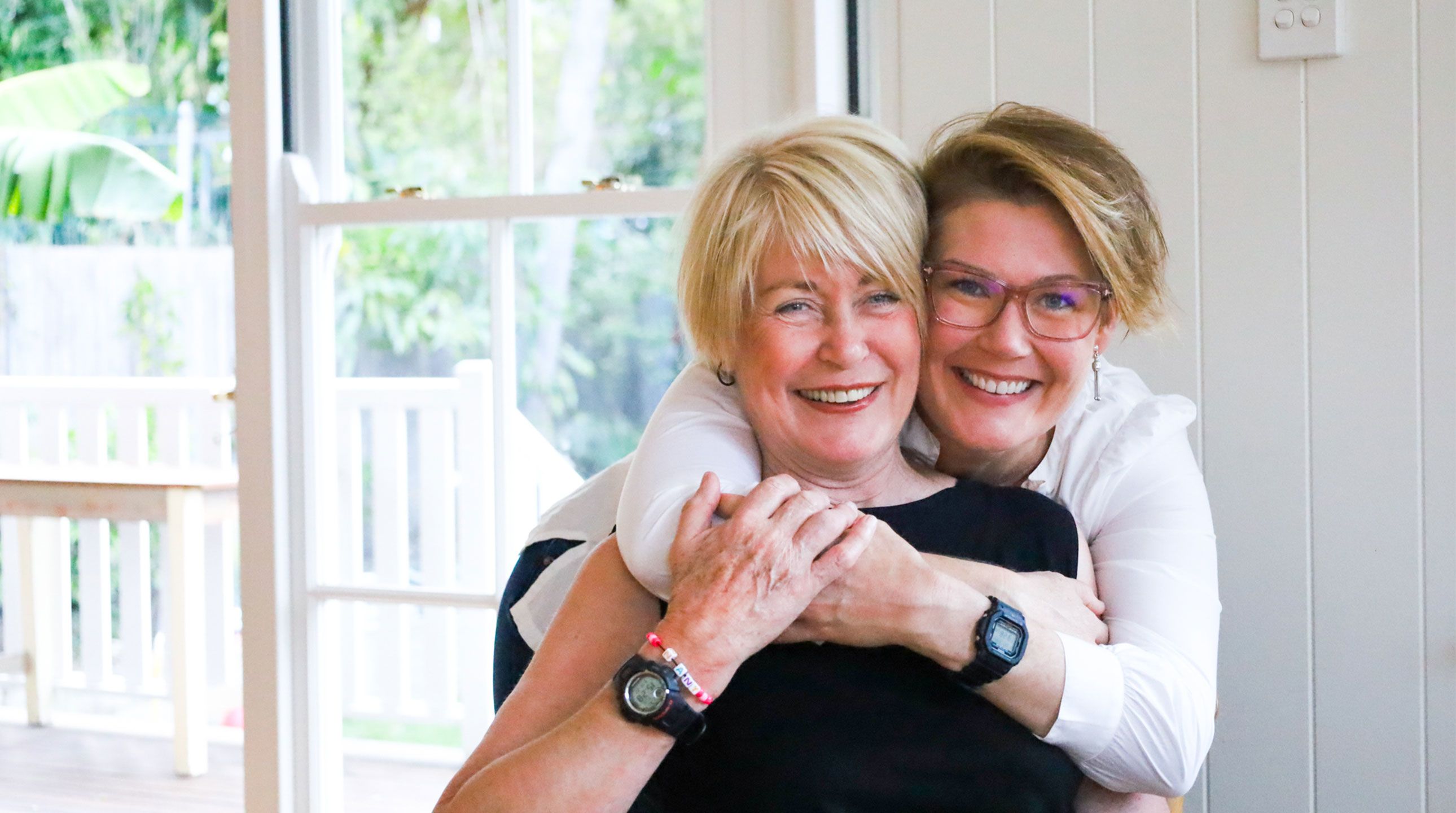 Two women share a hug and smile towards the camera.