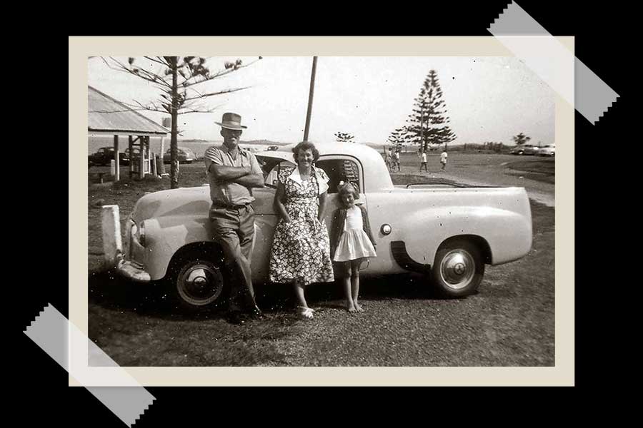 An image of Judith Anderson standing with her father Ralph Brown and mother Amy in front of the family's FX Holden ute on holiday at Southport in the mid-1950s.
