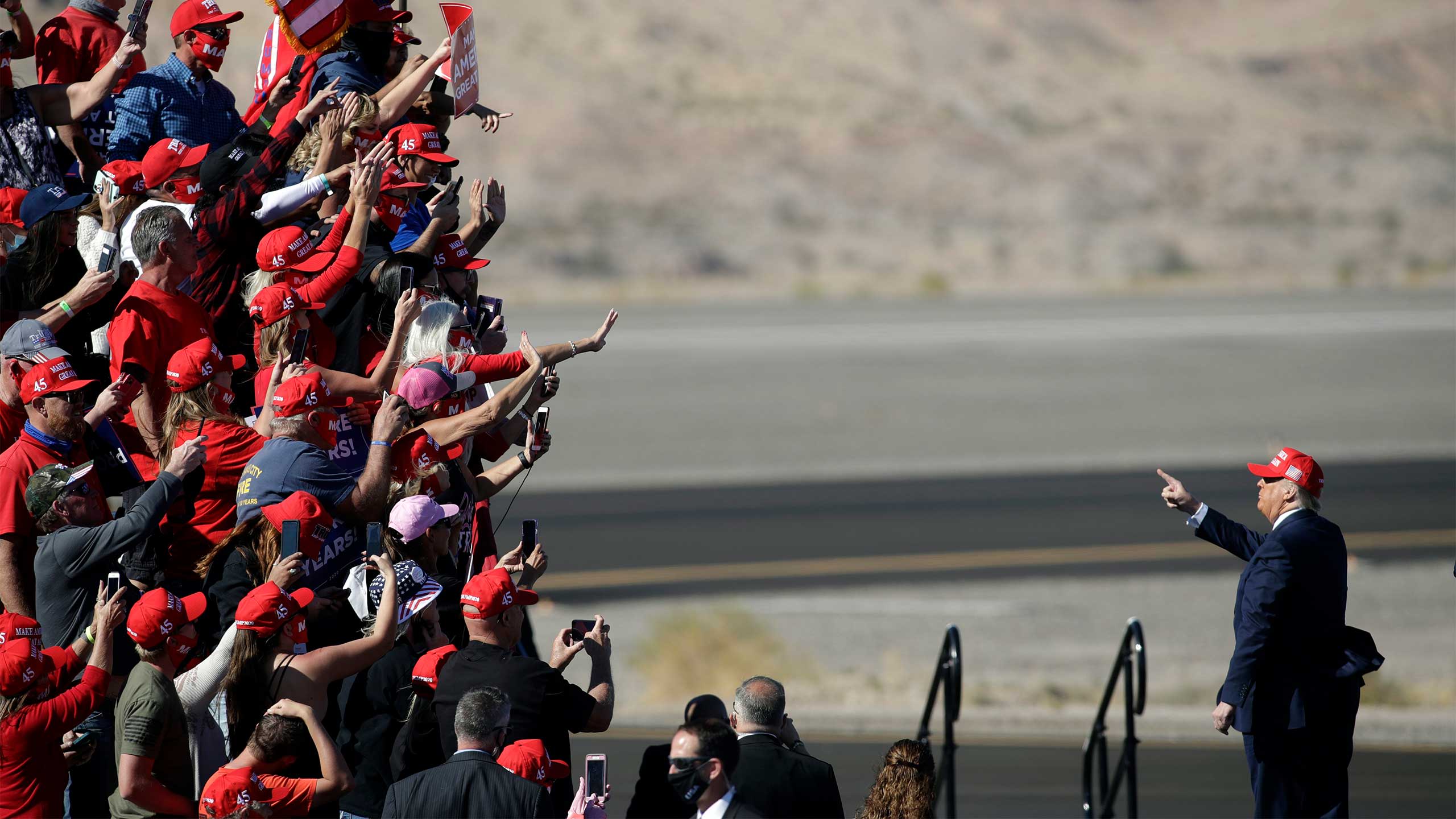 An image of Donald Trump addressing his supporters at a rally. Trump and the supporters are wearing red 'Make America Great Again' hats.