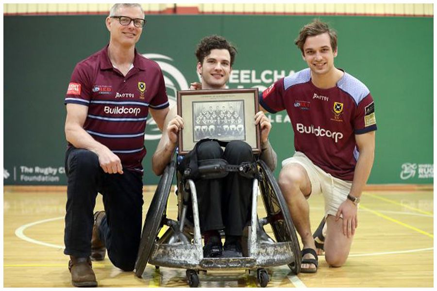 An image of Conor Tweedy, with father Sean and brother Seamus, holding a photo of his grandfather's UQ Rugby premiership-winning side.