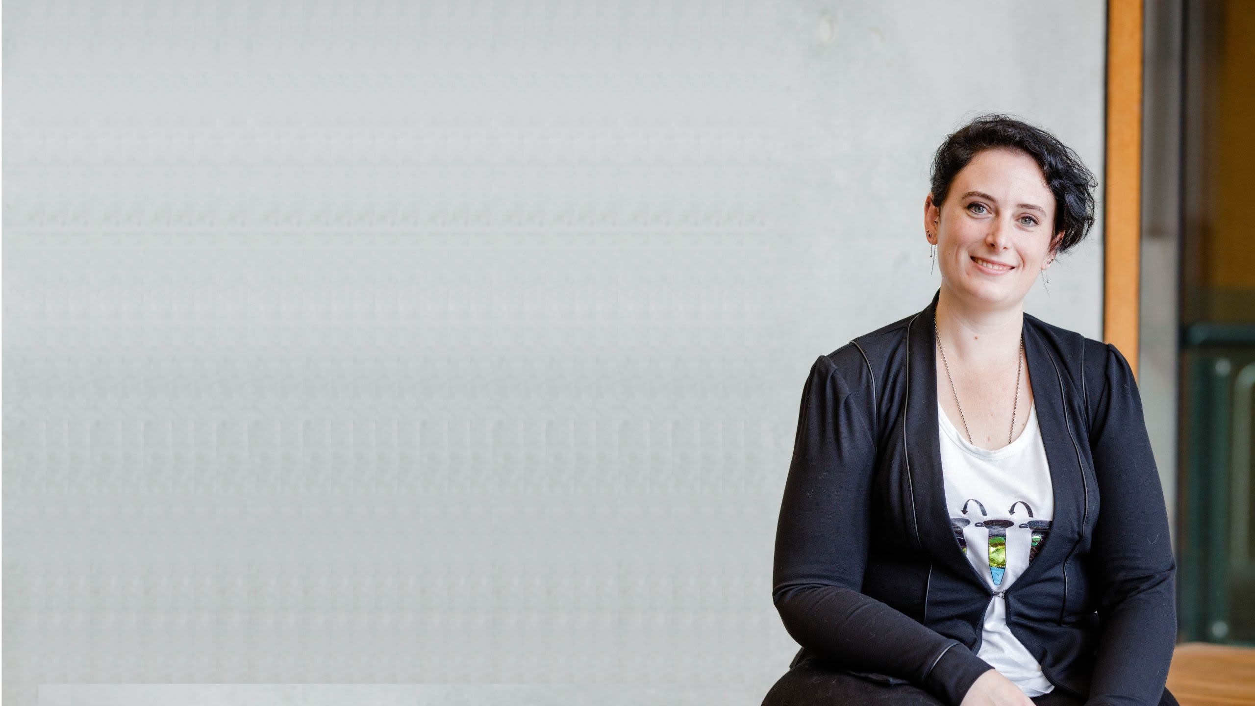Chris Pymble sits in front of a grey background wearing a black blazer. She's smiling at the camera.