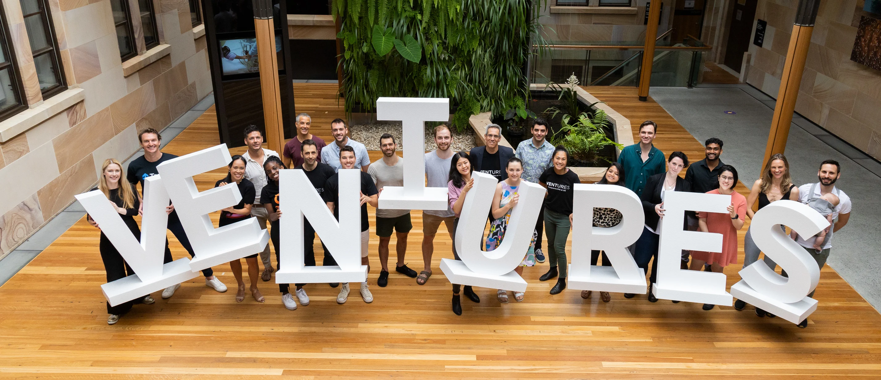 2022 UQ Ventures iLab Accelerator participants standing in the Create Change Institute foyer holding large white letter that read, Ventures.