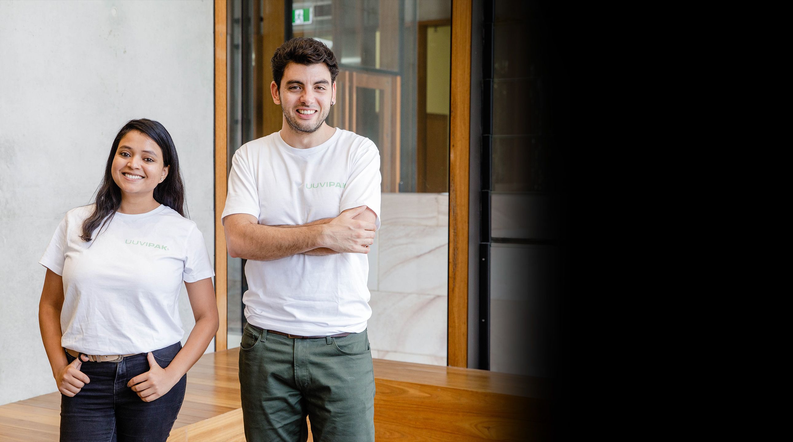 Dr Shafali Gupta and Andy Epifani stand wearing white t-shirts with their company logo on it smiling at the camera. Shafali is on the left with her hands in her pockets and Andy has his arms crossed and is on the right of the photo.
