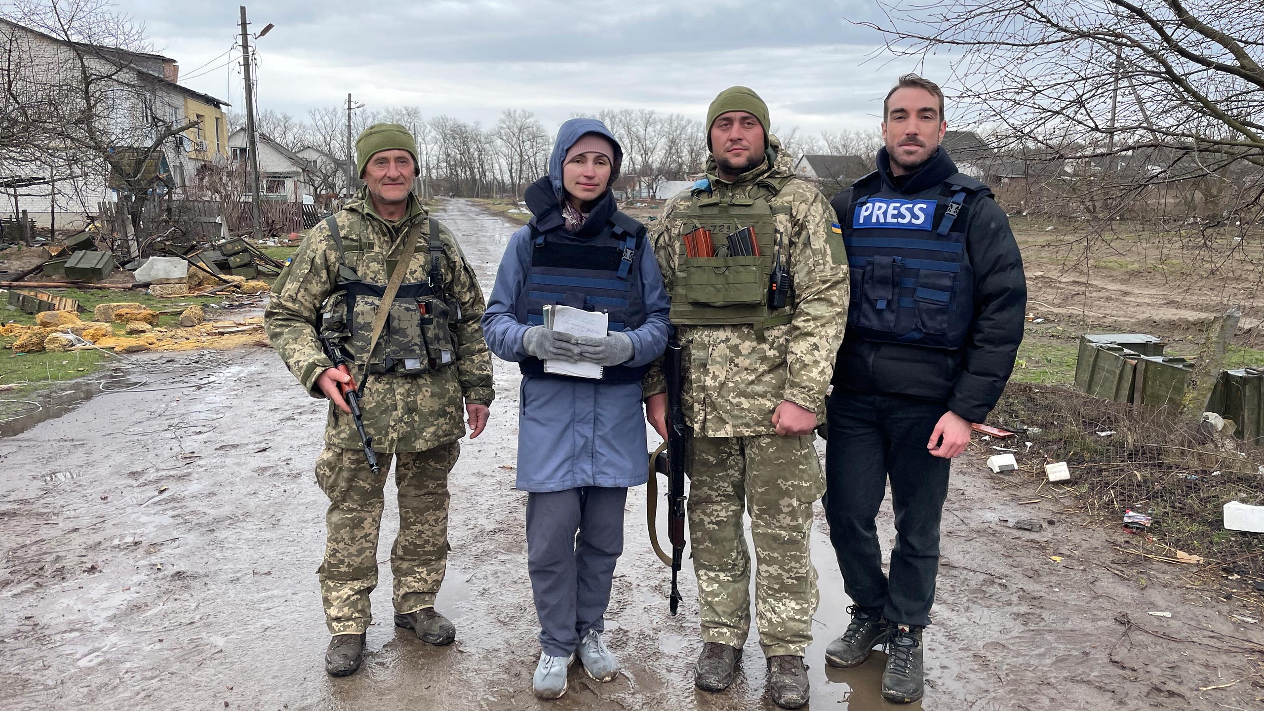 Two armed soldiers stand with two journalists in press flak jackets.