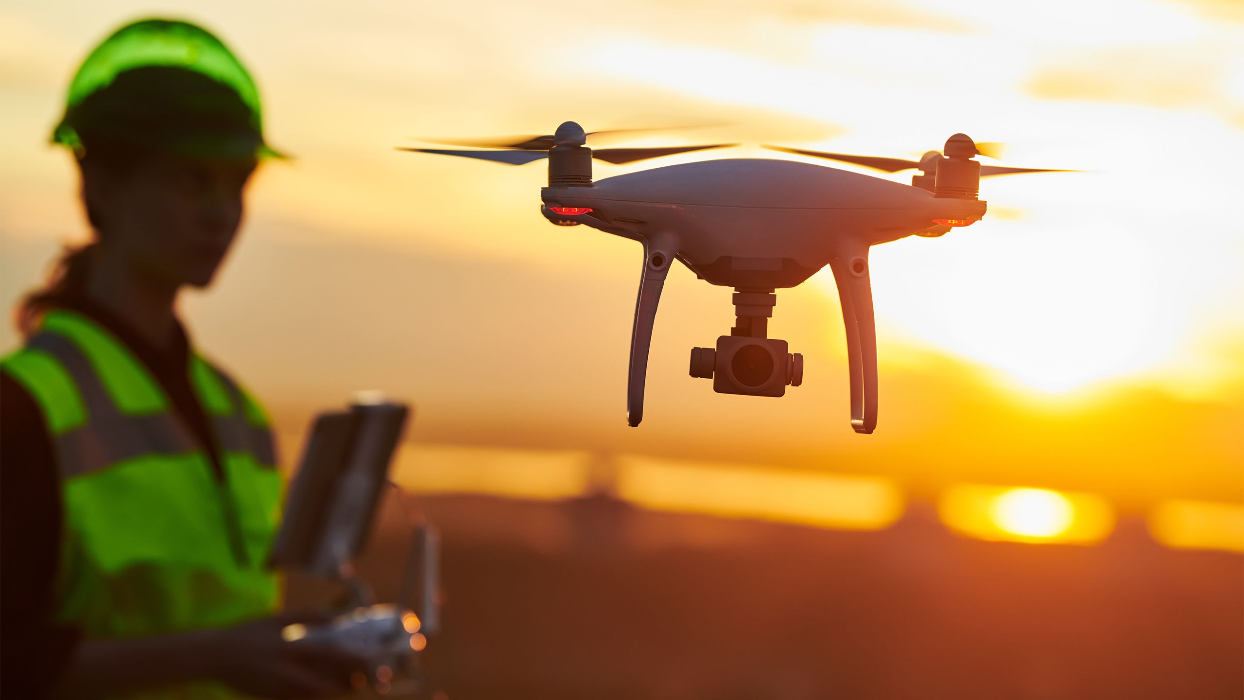 A drone pilot flying a drone on a construction site at sunset.