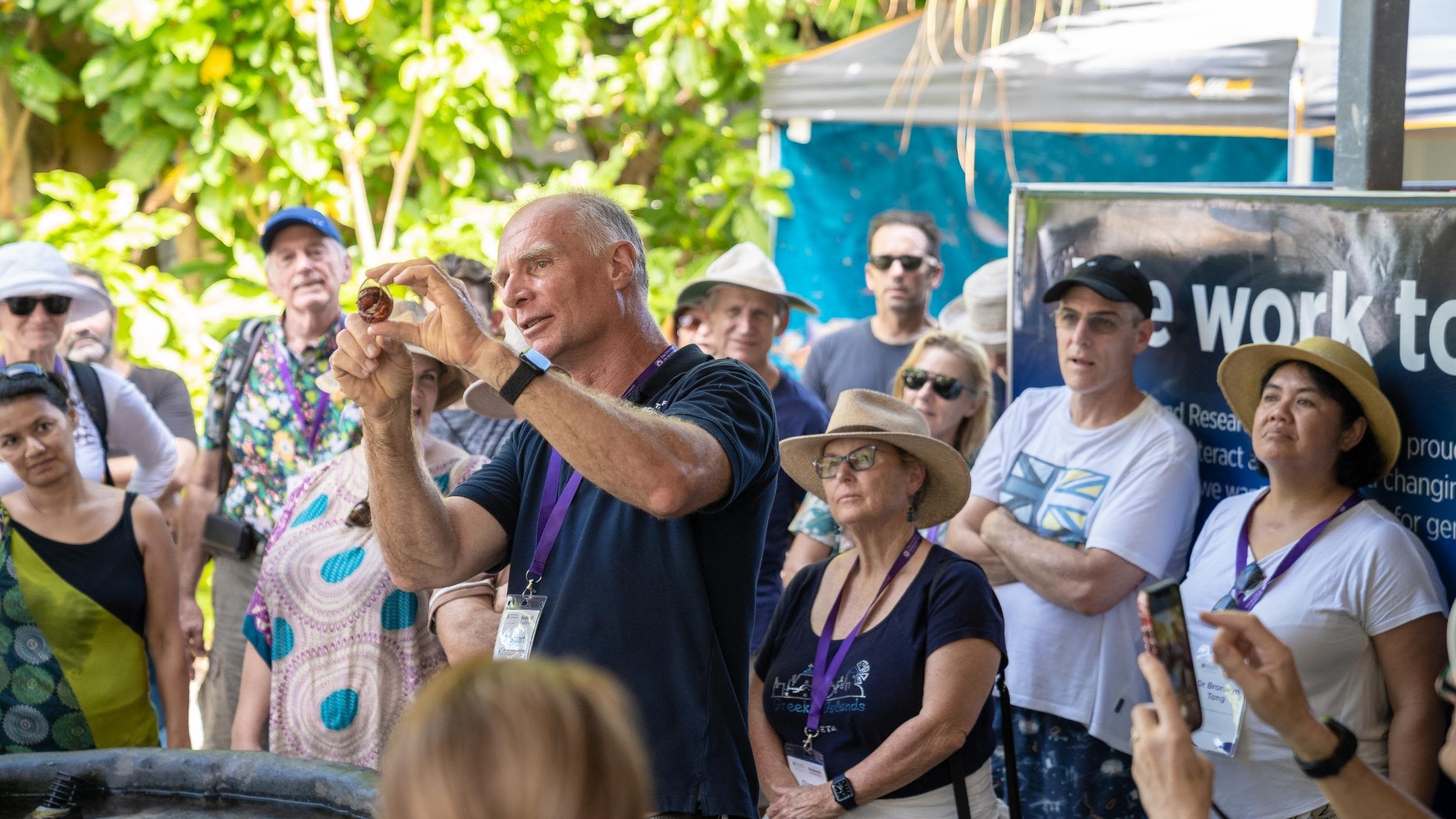 A man holds up a shell to demonstrate marine creatures to a large audience 