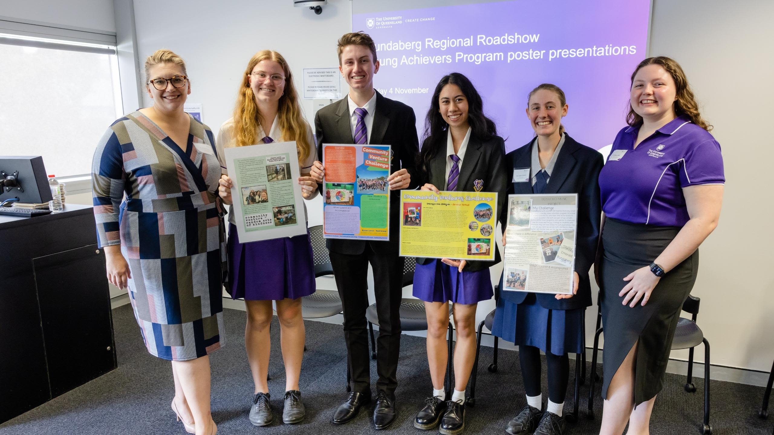 4 high school students stand with two women from the University, holding posters that show their community presentations
