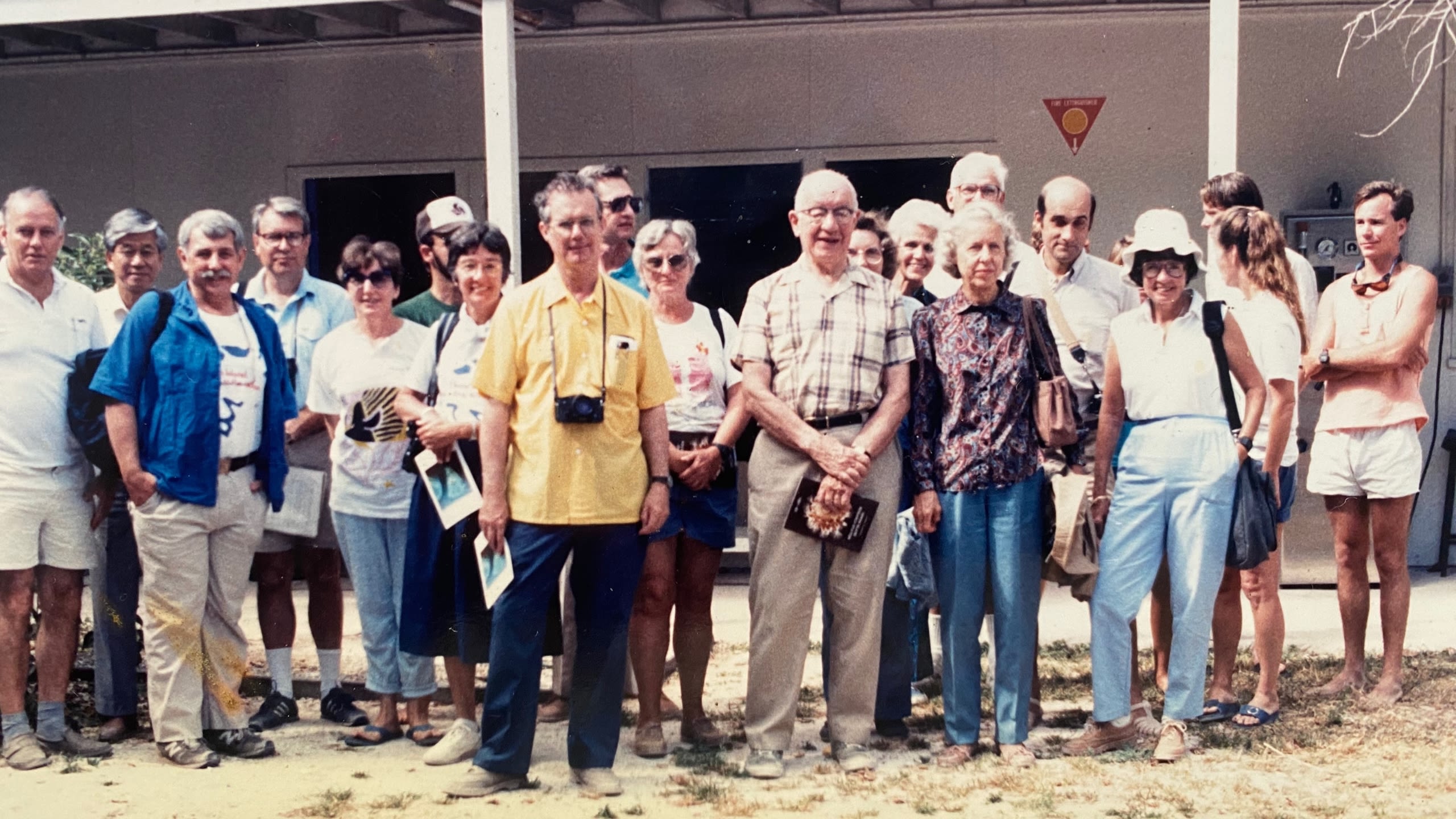 A large group of people from diverse ages and genders stand outside a building on Heron island and smile for the camera