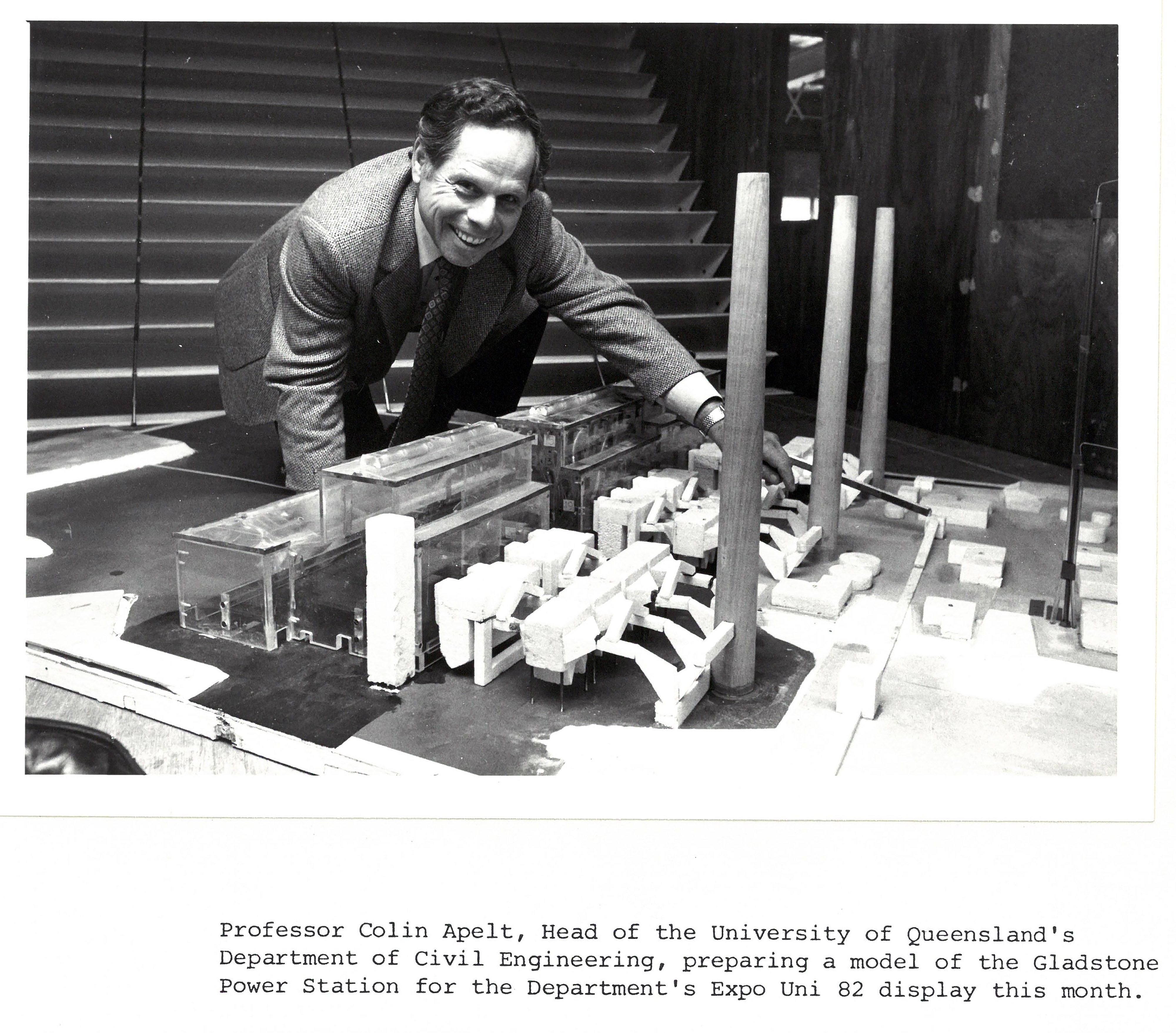 A black and white photo of a man in a suit and tie standing over a small model power station