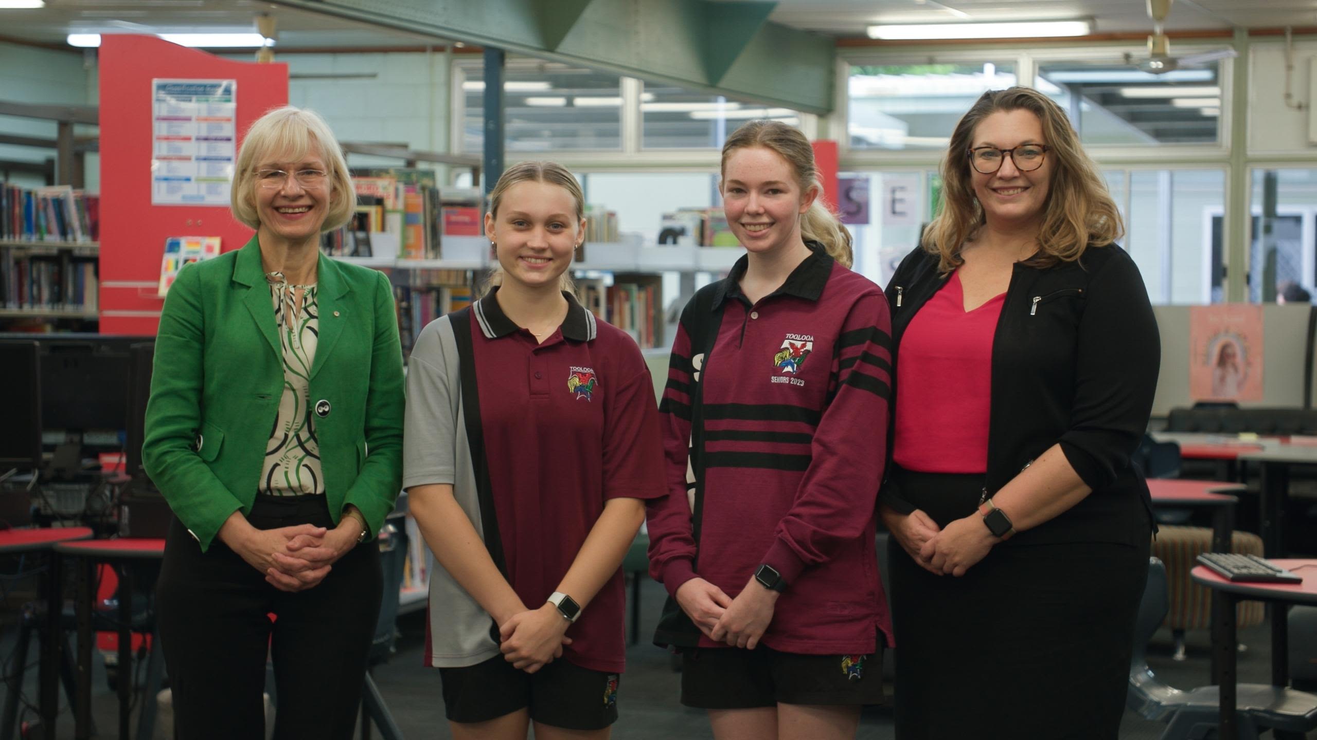 2 high school students in maroon school uniforms stands with two women from the University of Queensland. They are all smiling at the camera.