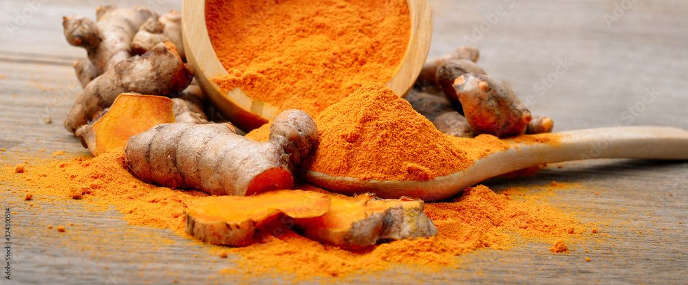 Whole and powdered turmeric on wooden benchtop