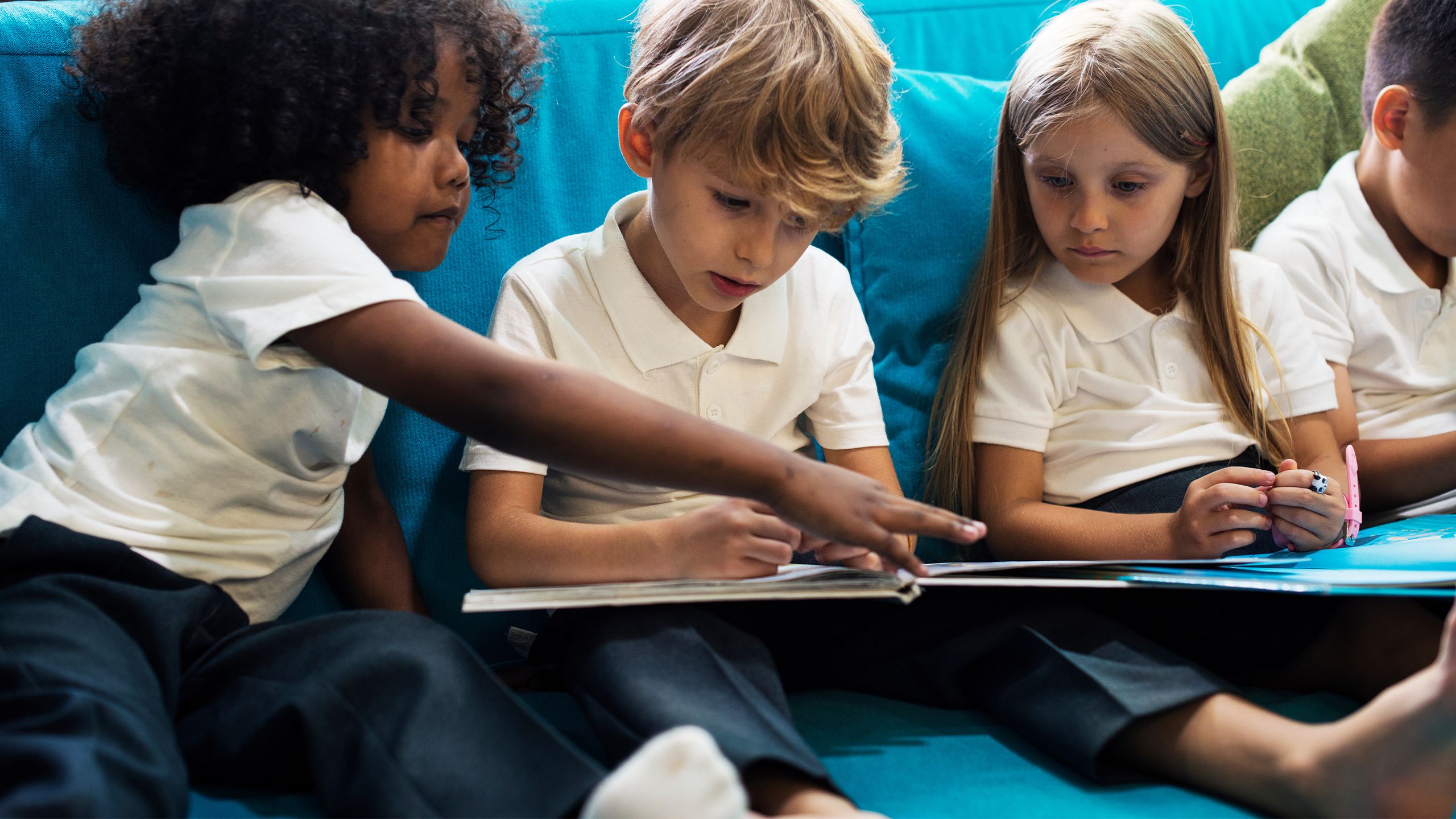 Young school children sitting and reading together on a couch at after school care.