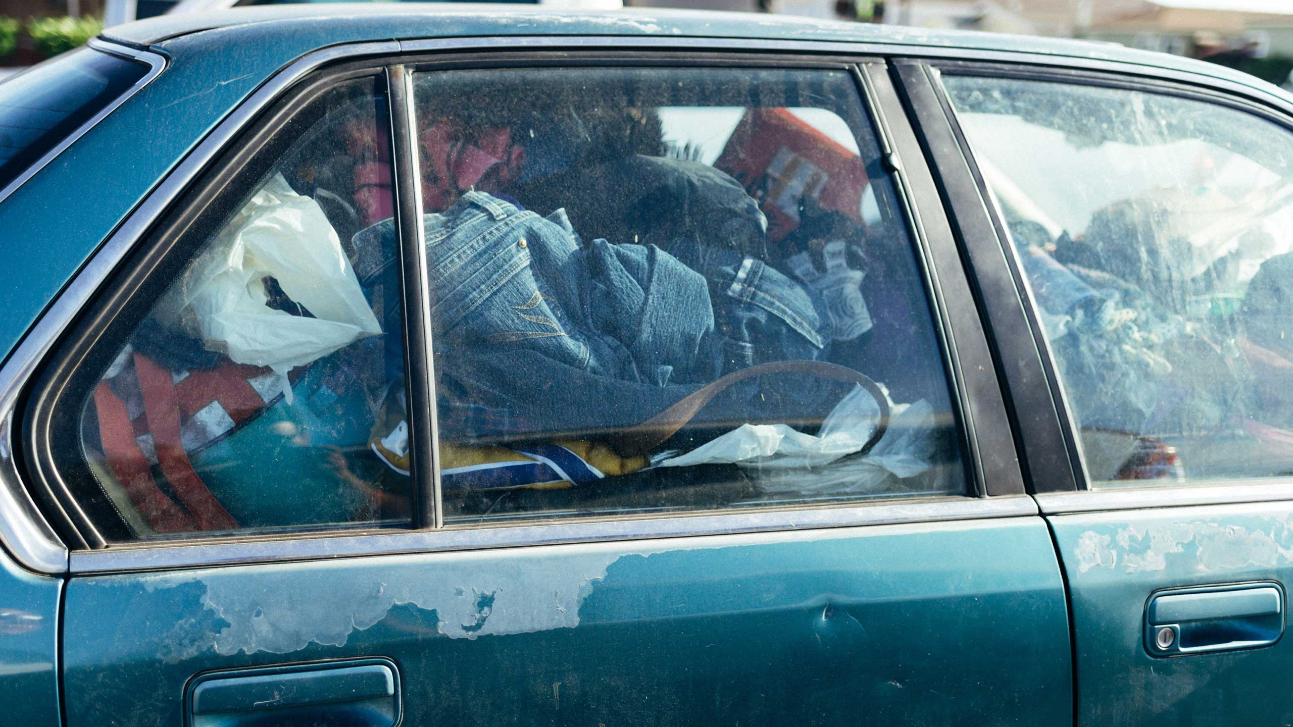 An image of an old, rusted car filled with clothes and other belongings inside.