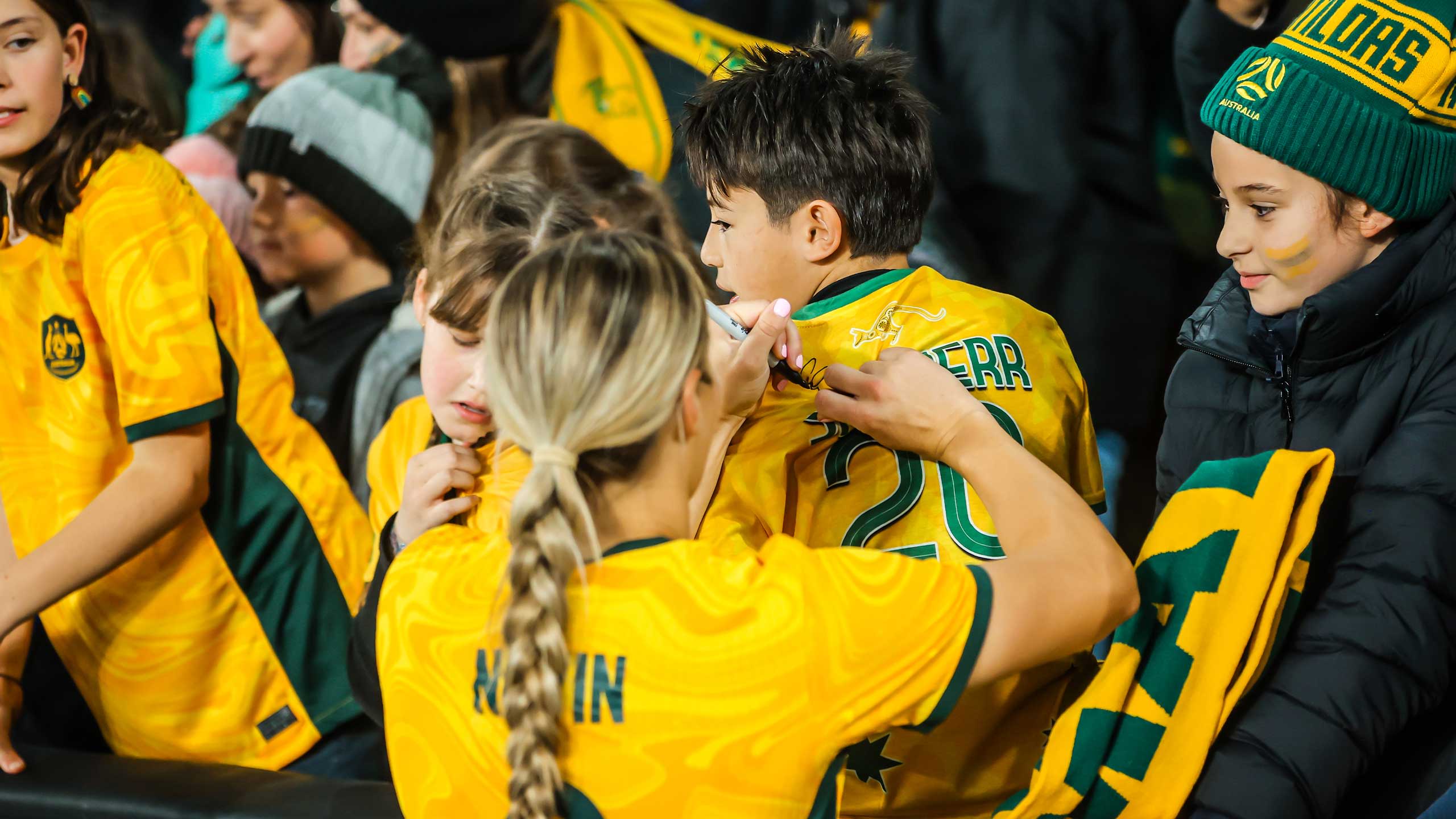 An image of Matildas players signing shirts of young fans after a match.