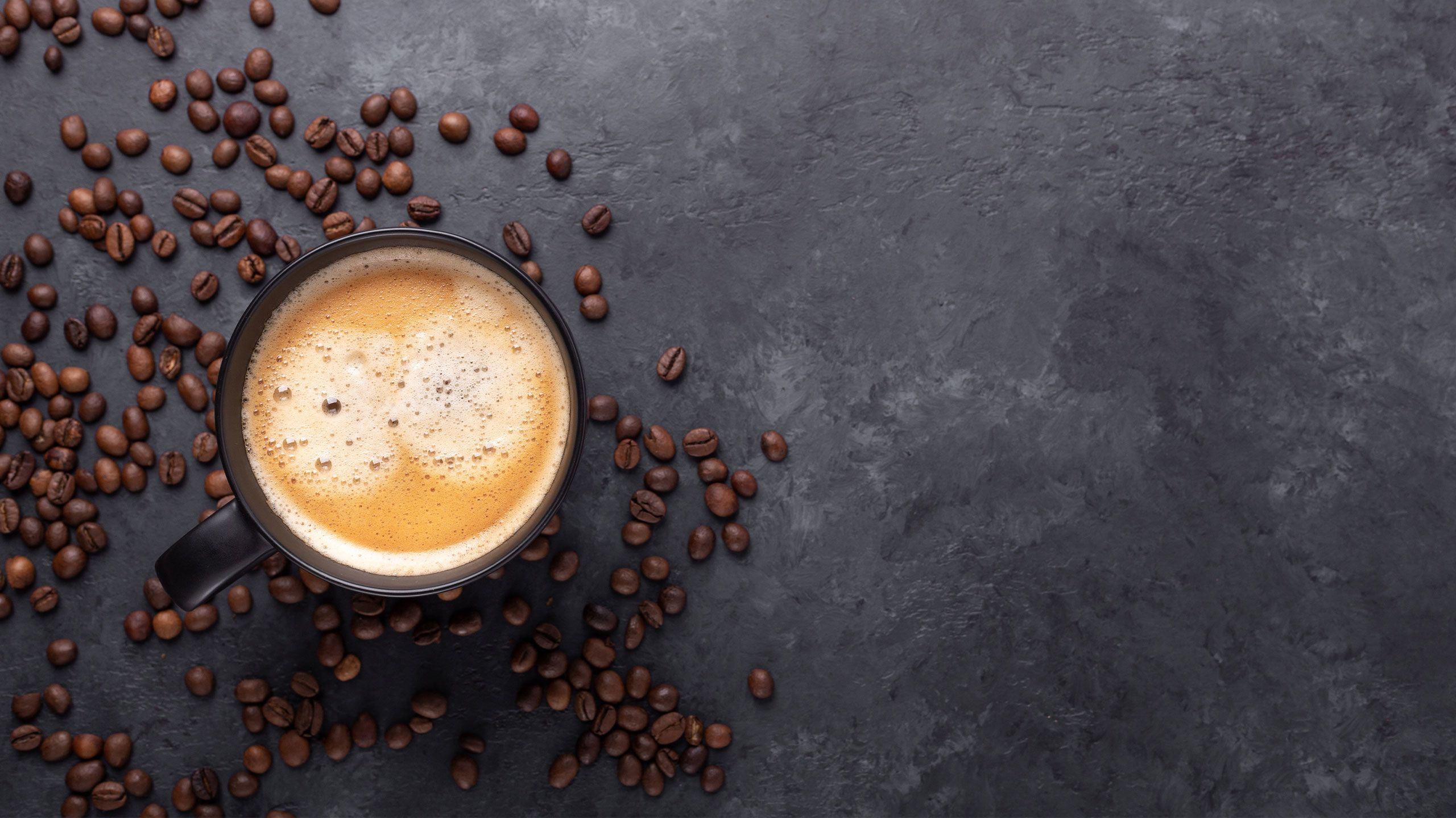 Cup of coffee and coffee beans on dark stone background.