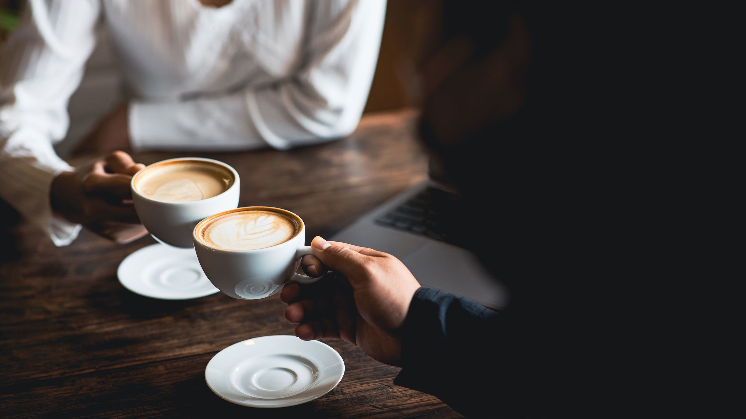 Close-up of a man and woman clinking a white coffee cup in a coffee shop.