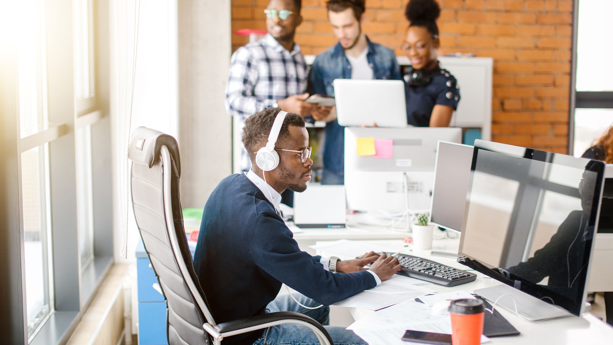 Office worker typing at his desk while wearing headphones because of the noisy room.