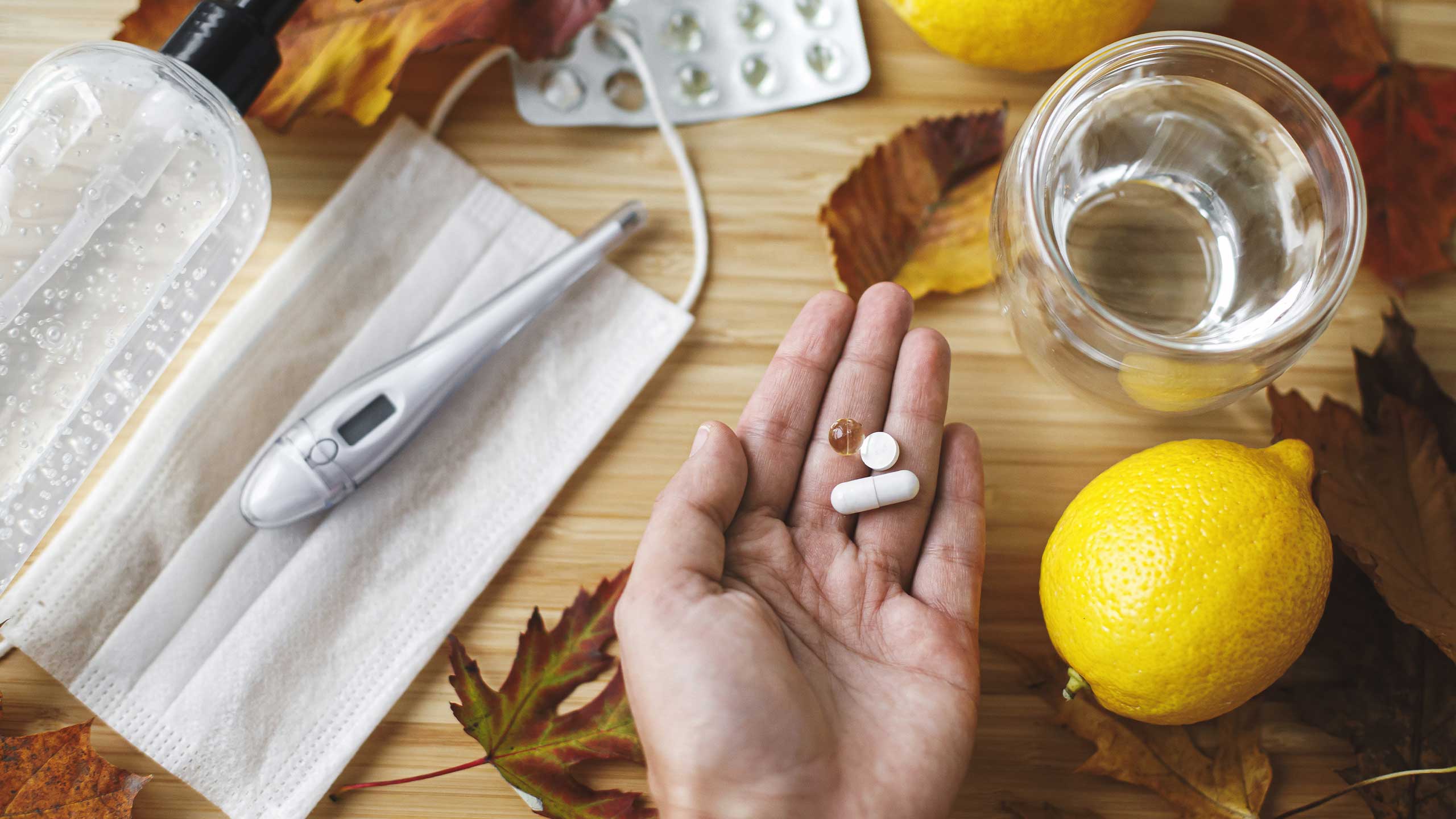 A hand holding vitamin tablets over a counter with lemons and other citrus fruit.