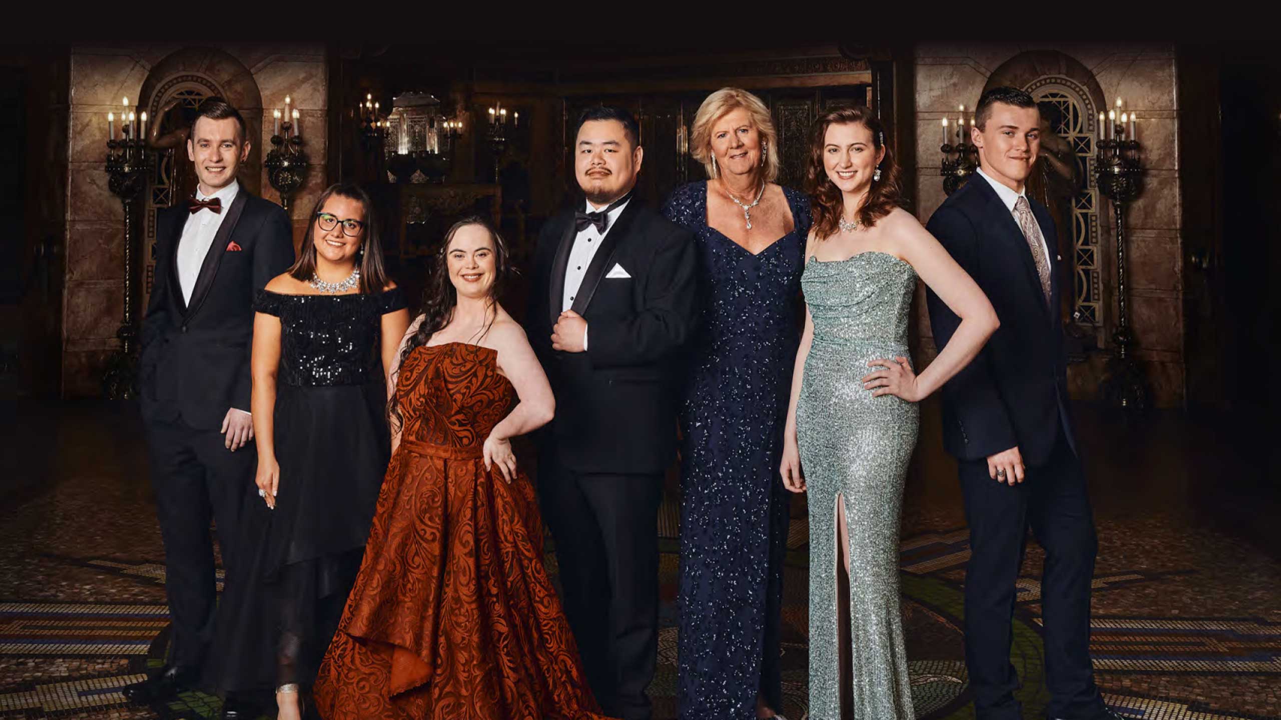 Image of seven people standing in a ball room they are all wearing formal attire