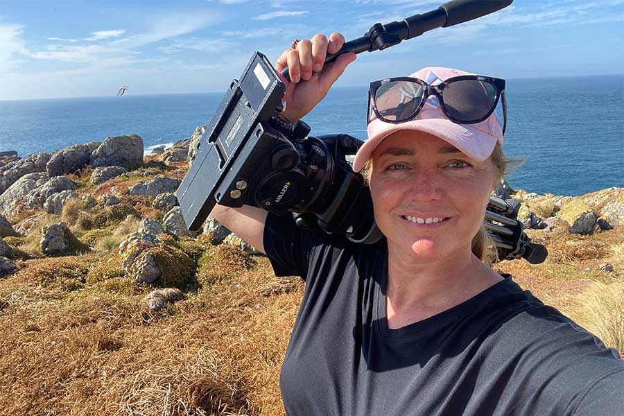 An image of Karina Holden with a video camera slung over her shoulder while filming on Albatross Island in north-west Tasmania.